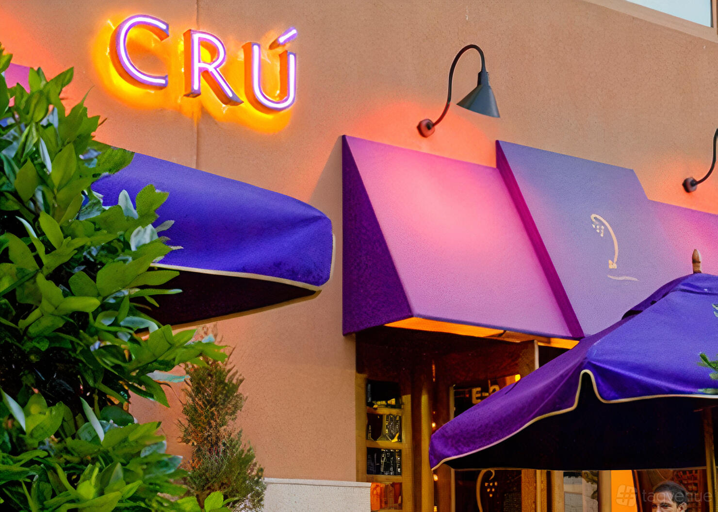 An exterior restaurant entrance with purple awnings, neon signage, and matching umbrellas at CRU Food & Wine Bar @ Shops at Legacy.