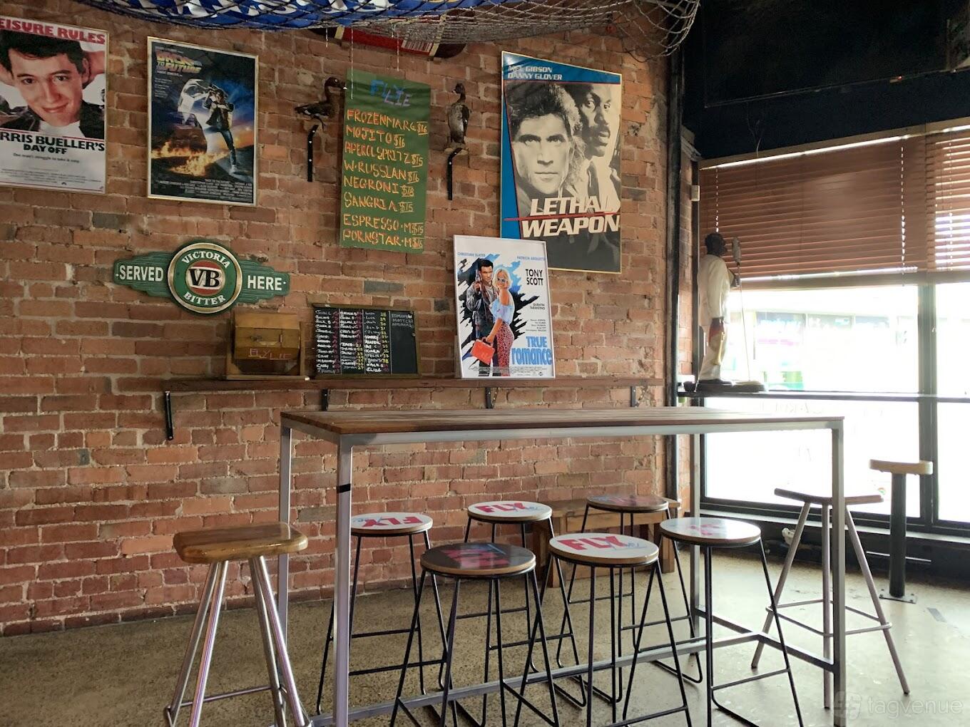 A bar with exposed brick walls, movie posters, high tables, and round stools at Fly Lie.