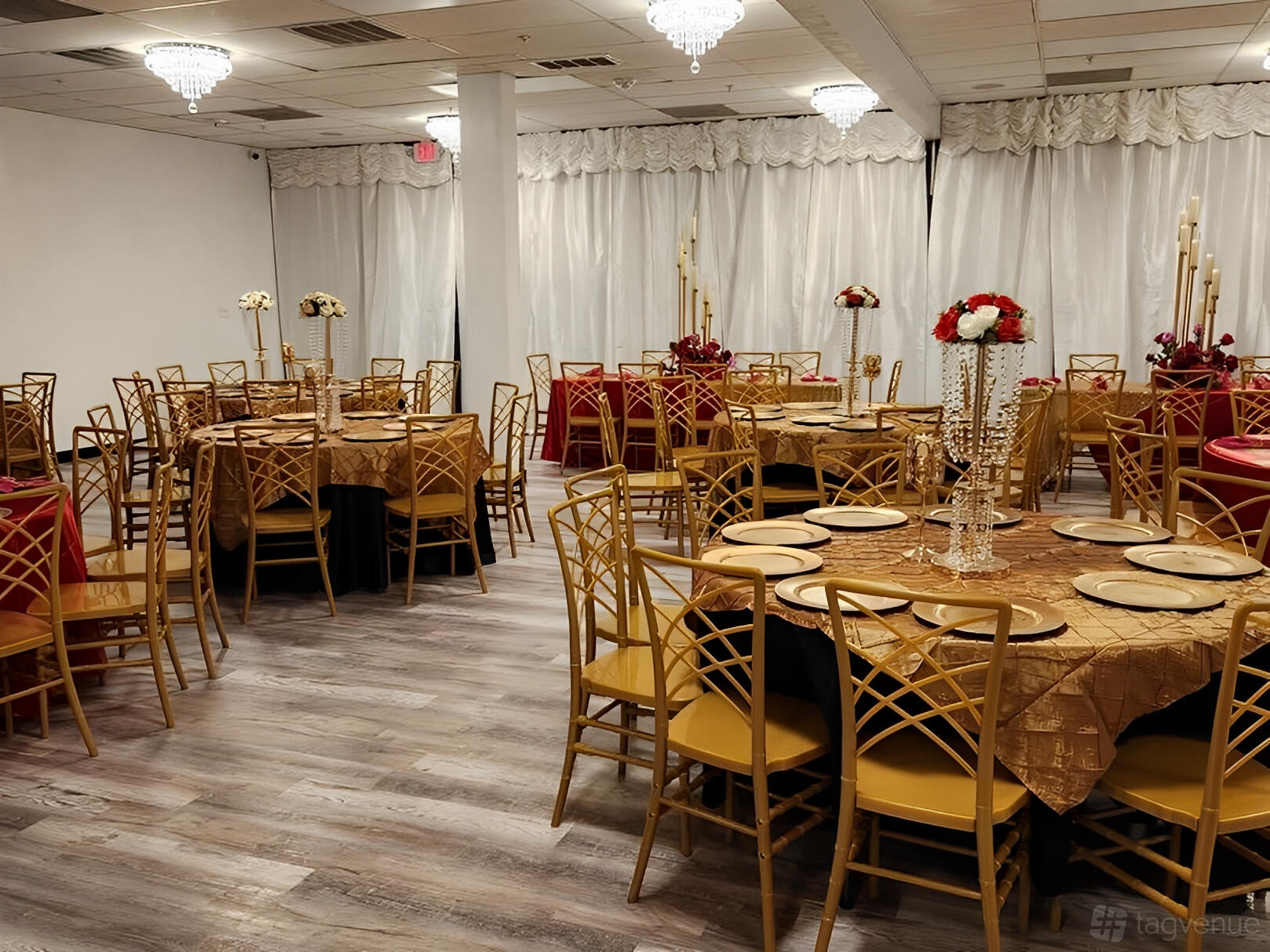 An event venue with gold chairs, round tables covered in gold and red linens, and crystal chandeliers at Bliss Pavilion 1.
