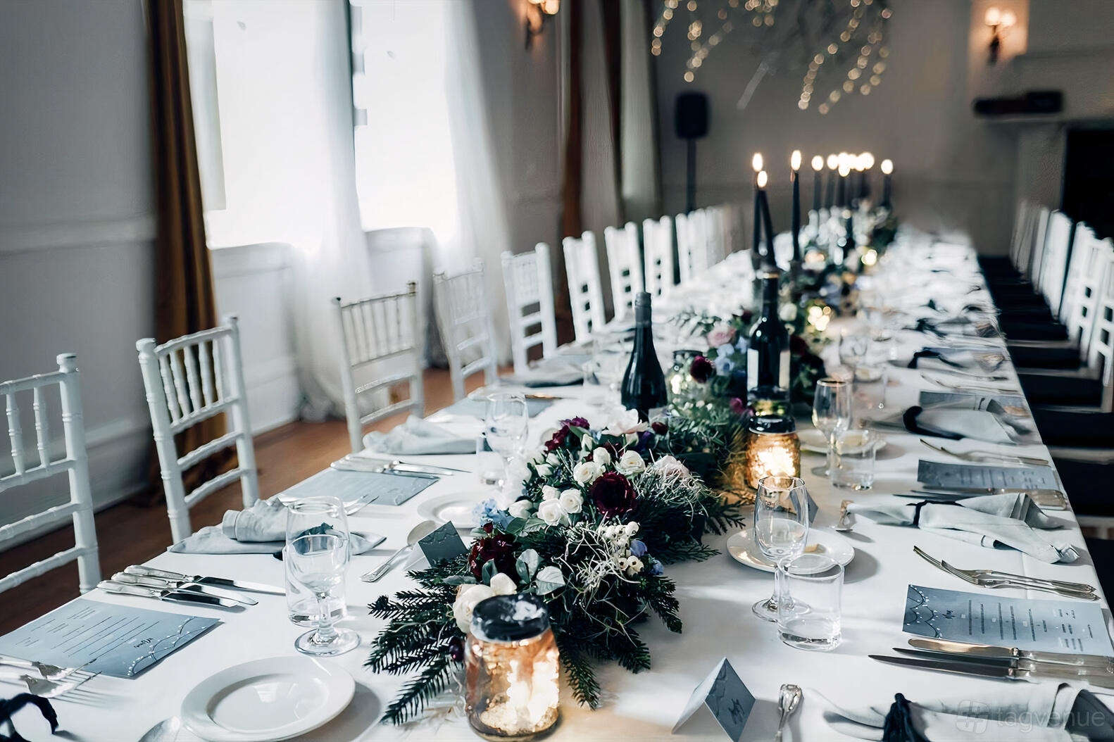 A hotel dining room with a long banquet table set with white linens, candles, floral centerpieces, and natural light at The Robertson Hotel.