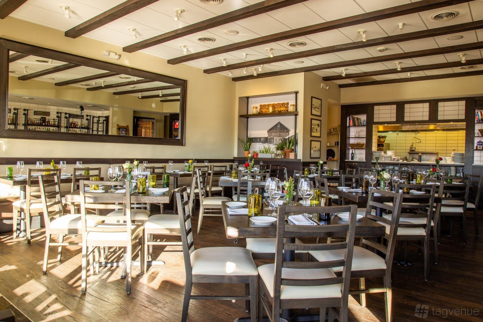 A restaurant dining room with wooden chairs, set tables, ceiling beams, and a large wall mirror at Prime Farm to Table.