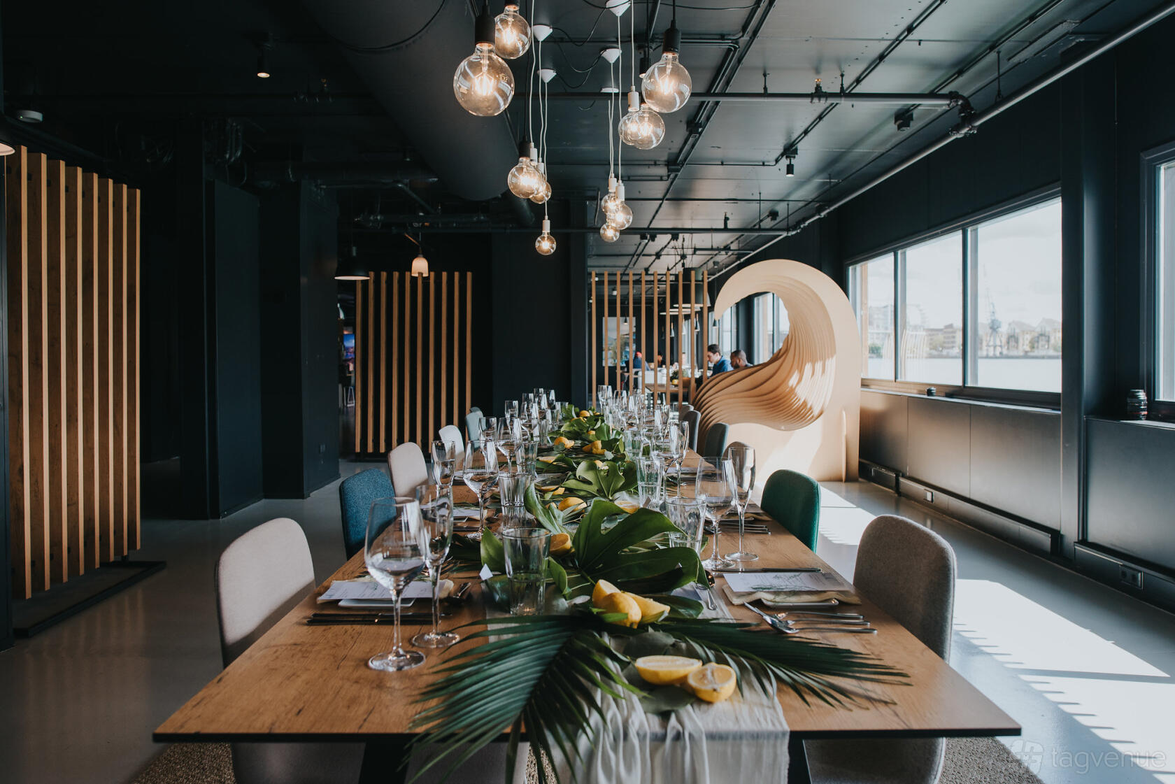 A hotel dining area with a long wooden table, pendant lights, and large windows at Good Hotel London