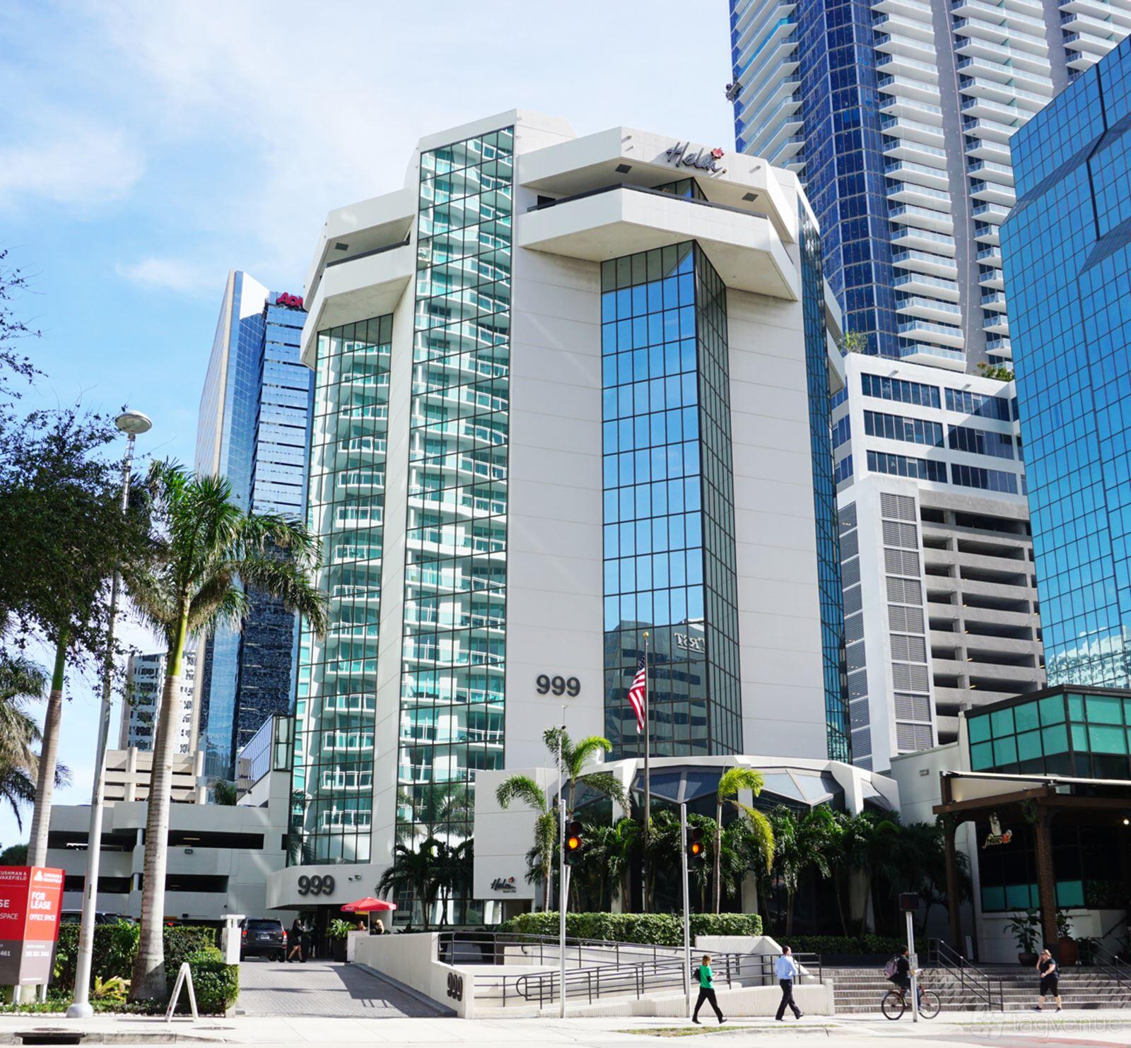 A meeting centre with a tall glass-fronted facade, palm trees, and an American flag at Office&Co. International Coworking.