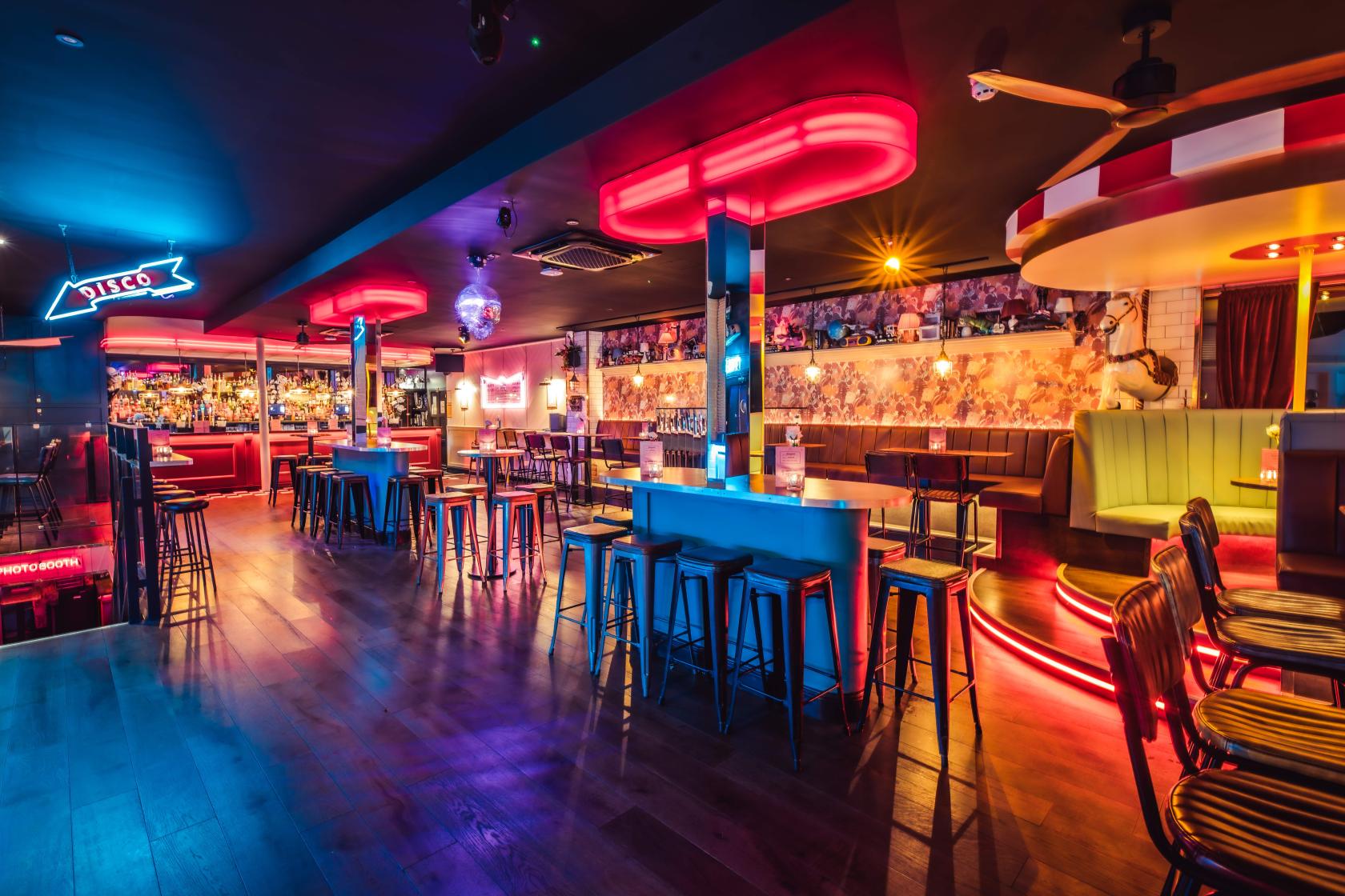 A cocktail bar with neon lighting, disco ball, colorful seating, and a long bar at Simmons | Shoreditch.