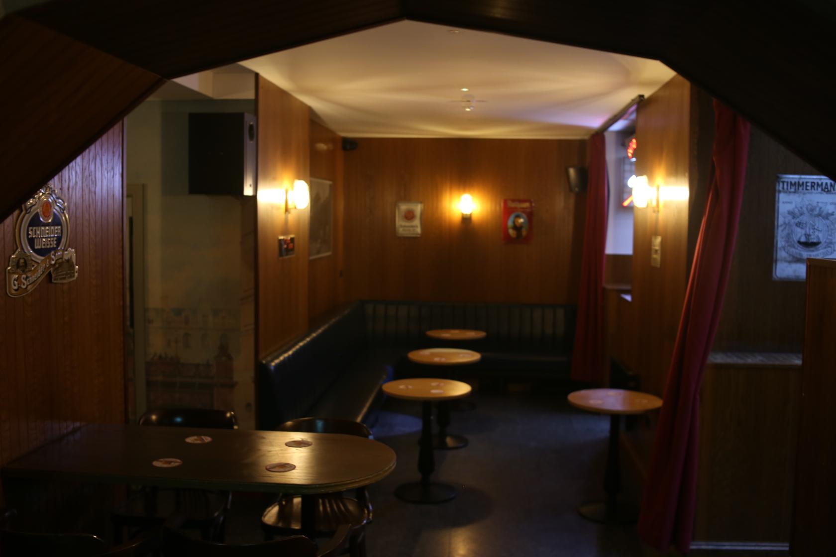 A basement pub space with wooden paneled walls, round tables, and wall-mounted lights at Farringdon Tap.
