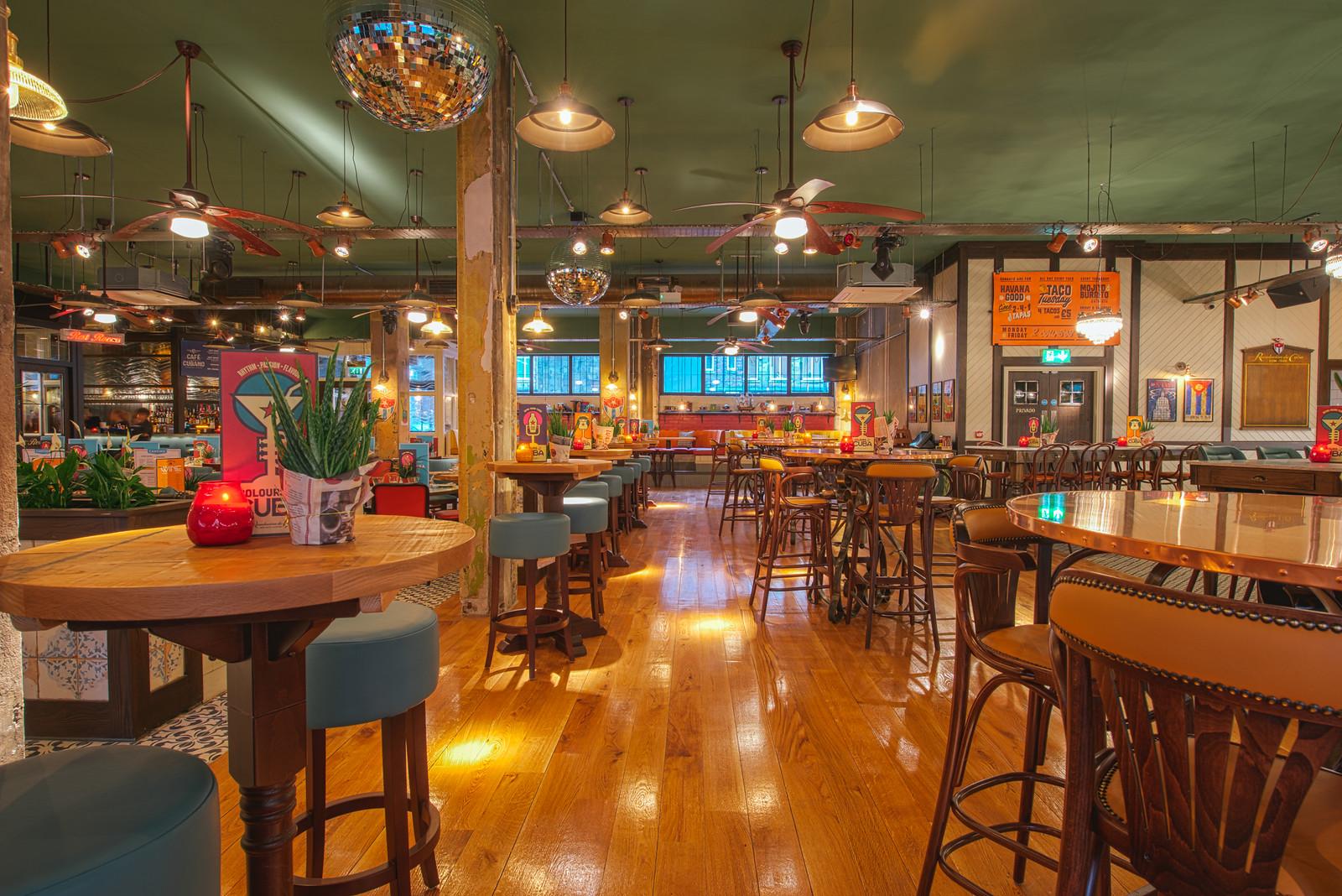 A bar with wooden floors, high-top tables, leather stools, and disco balls at Revolucion de Cuba Reading.