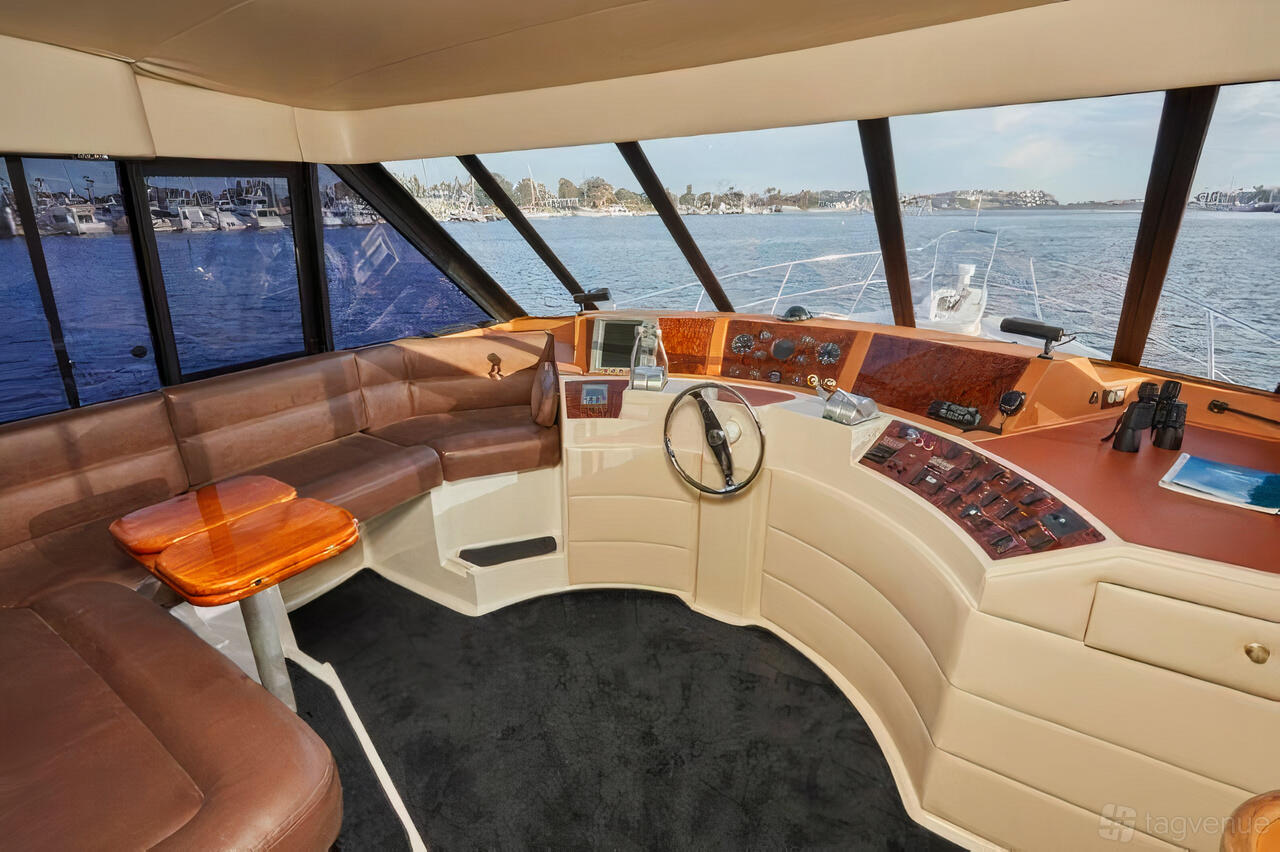 A yacht interior with wraparound leather seating, large windows, and a wood-accented helm at Luxury Yacht Charter.
