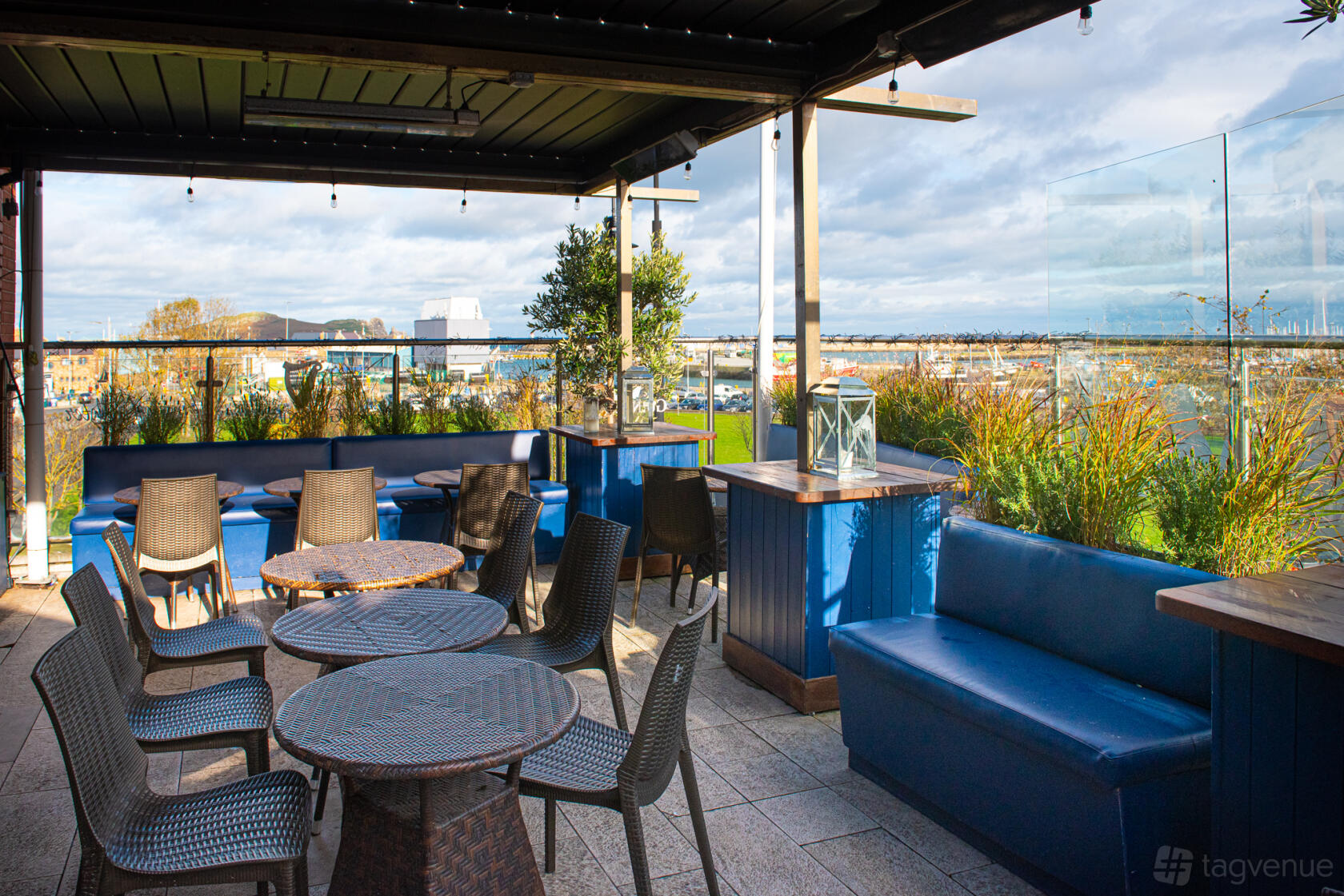 An outdoor bar area with wicker chairs, blue cushioned benches, and glass panel railings at Wrights Findlater Howth.
