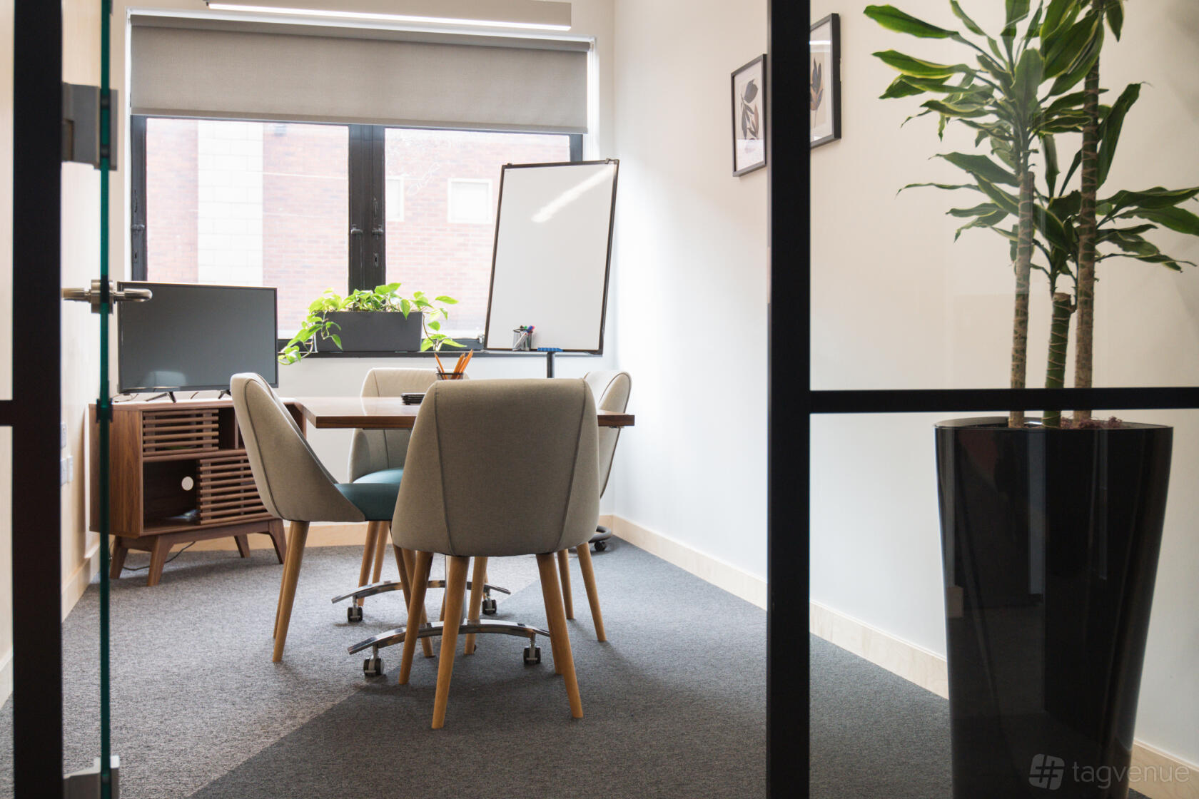 A meeting room with a round table, upholstered chairs, a large potted plant, and a whiteboard at Wizu Workspace - Sheffield - Eyre Street.