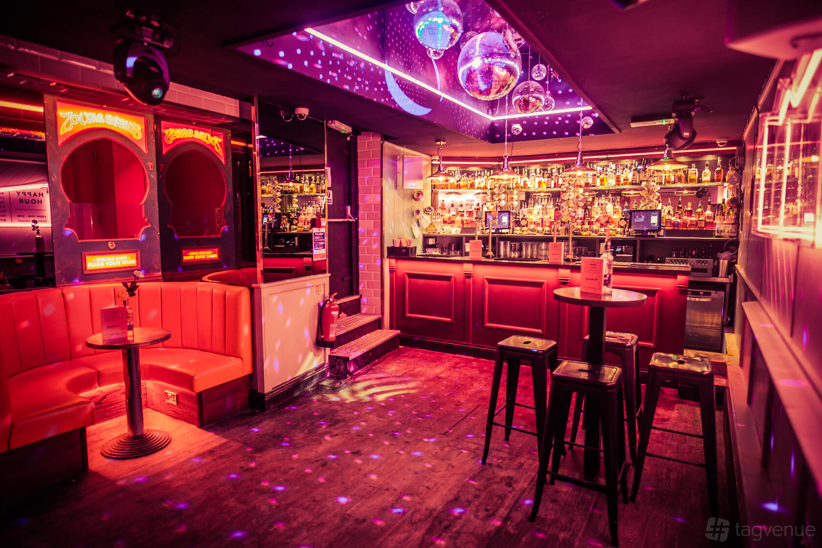 A cocktail bar with vibrant purple lighting, disco balls, and red booth seating at Simmons | Tottenham Court road.
