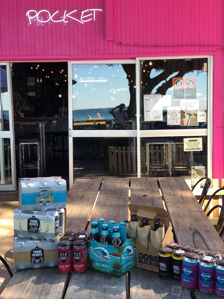 A pub with a wooden outdoor table, bottled beers, and glass doors leading to Pocket Bar.