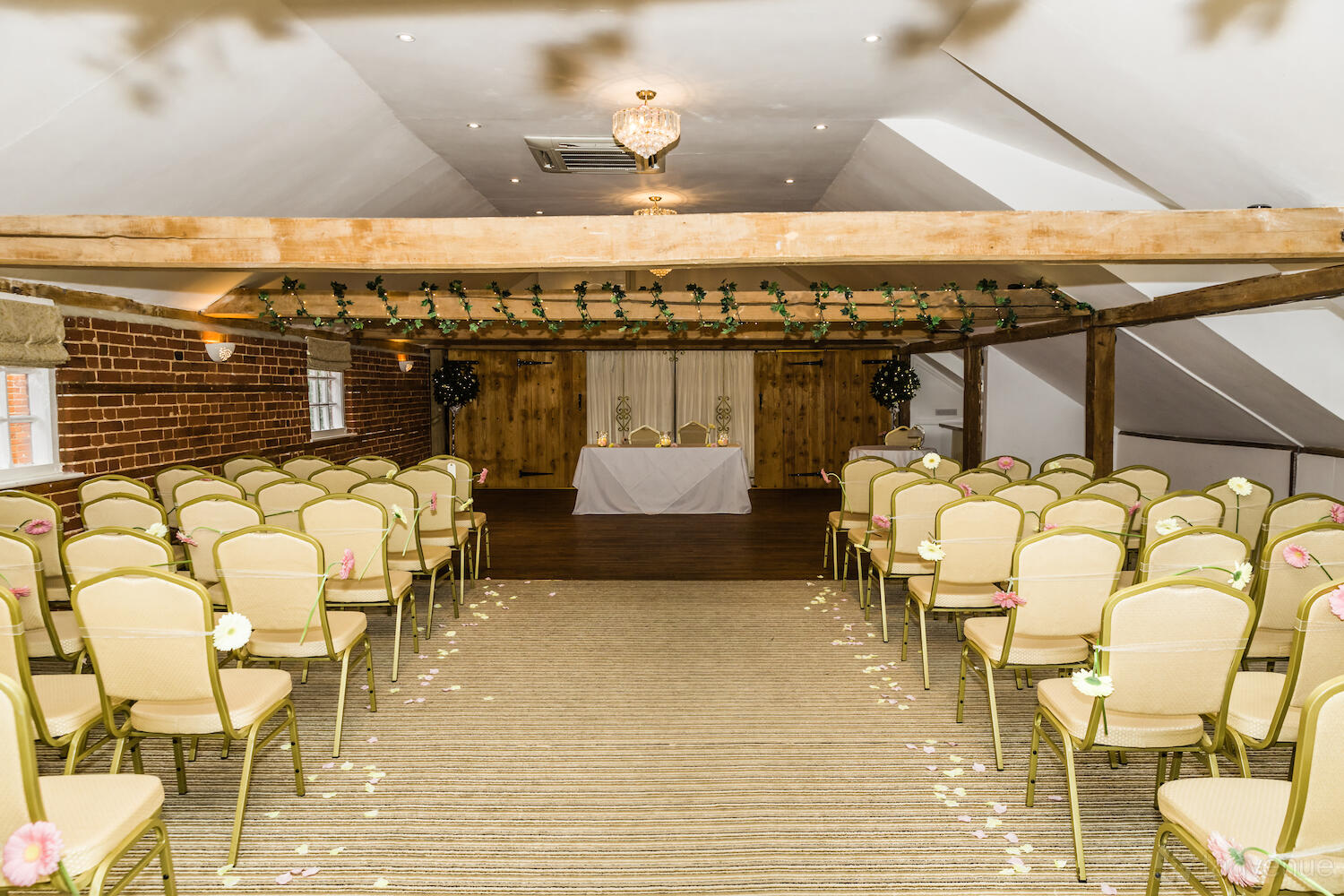 An event venue with exposed beams, brick walls, and rows of chairs with floral accents at The Venue at Kersey Mill.