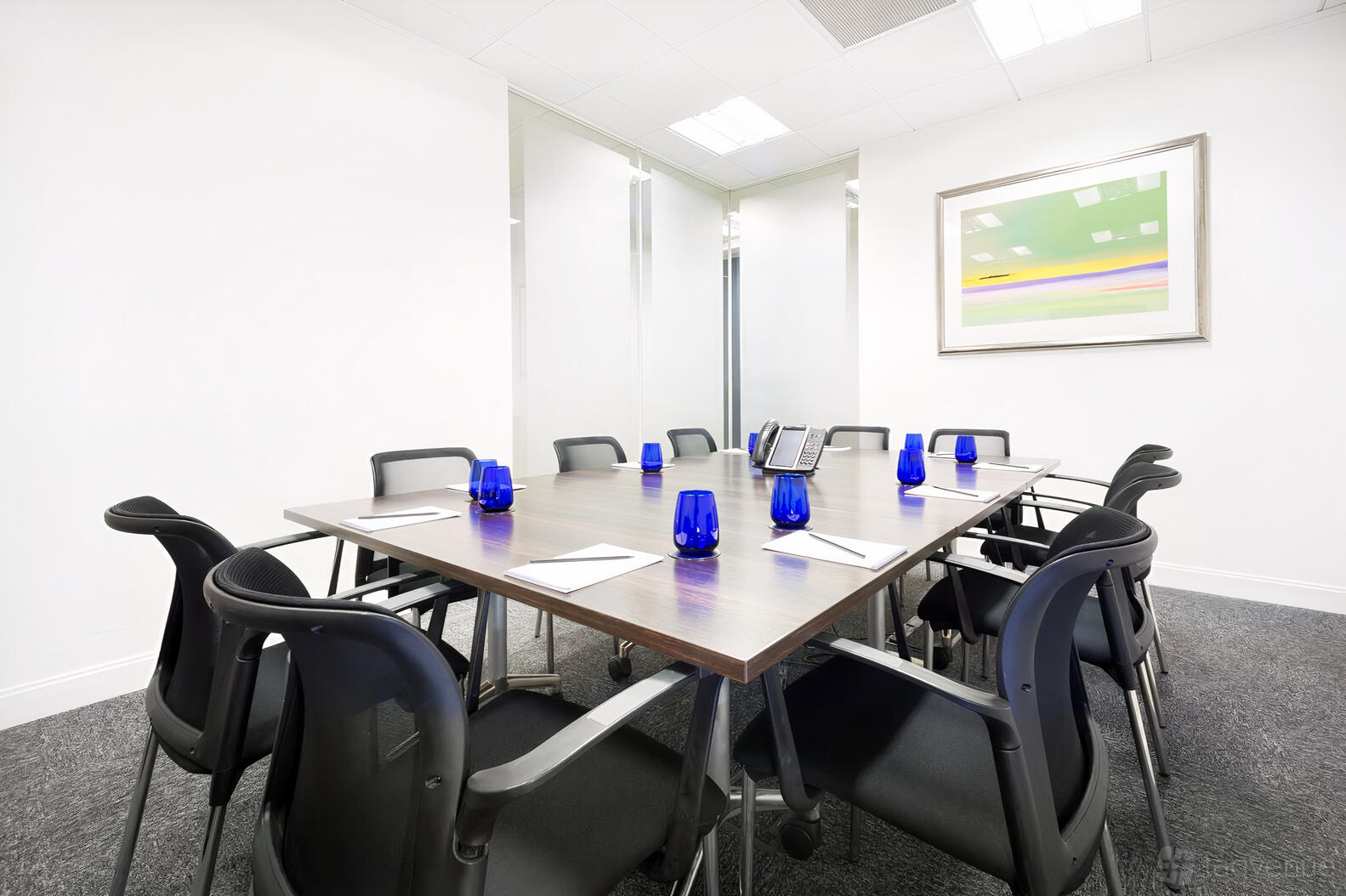 A meeting room with a large rectangular table, black chairs, blue water glasses, and modern artwork at Landmark: Brindleyplace, Birmingham.