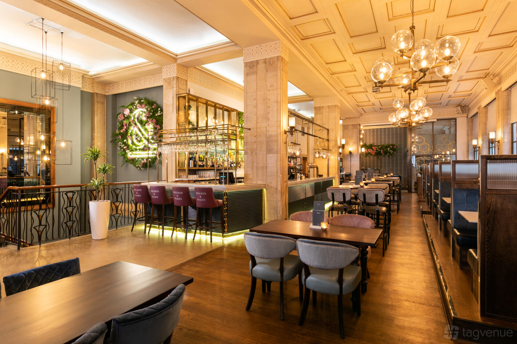 A bar with a central illuminated counter, hanging glass chandeliers, and floral wall decor at Pitcher & Piano Cornhill.