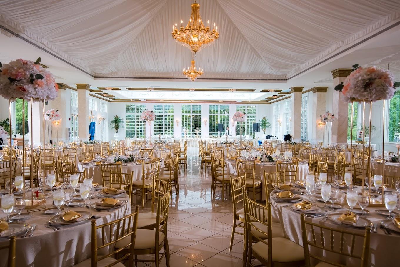 An event venue with gold chiavari chairs, round tables set with floral centerpieces, and a grand chandelier at The Haley Mansion.