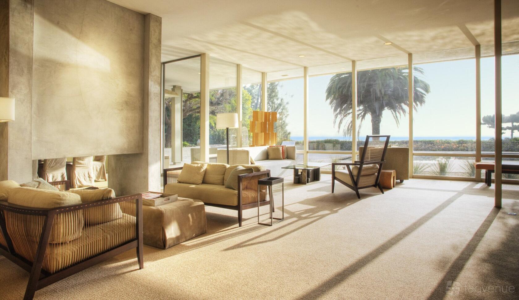 A house living area with floor-to-ceiling windows, beige carpeting, and modern seating at The Cresthill Villa.