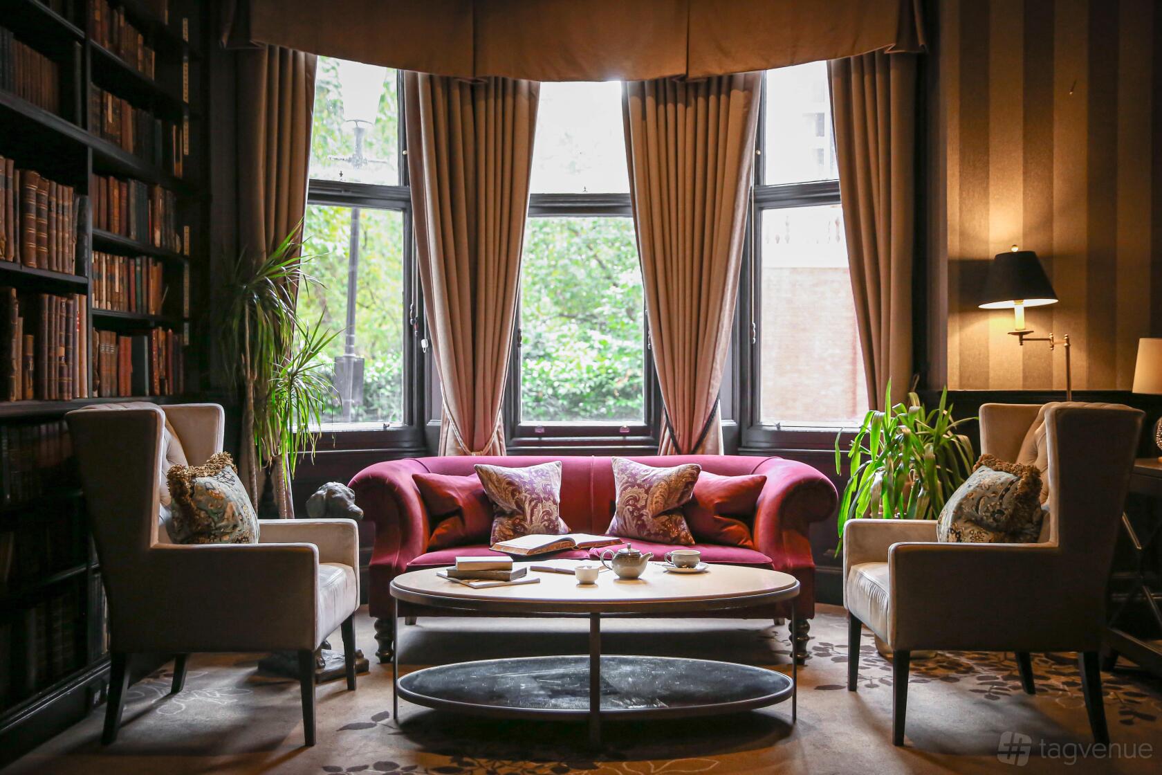 An event space with tall bookshelves, armchairs, and a red velvet sofa by bay windows at 11 Cadogan Gardens