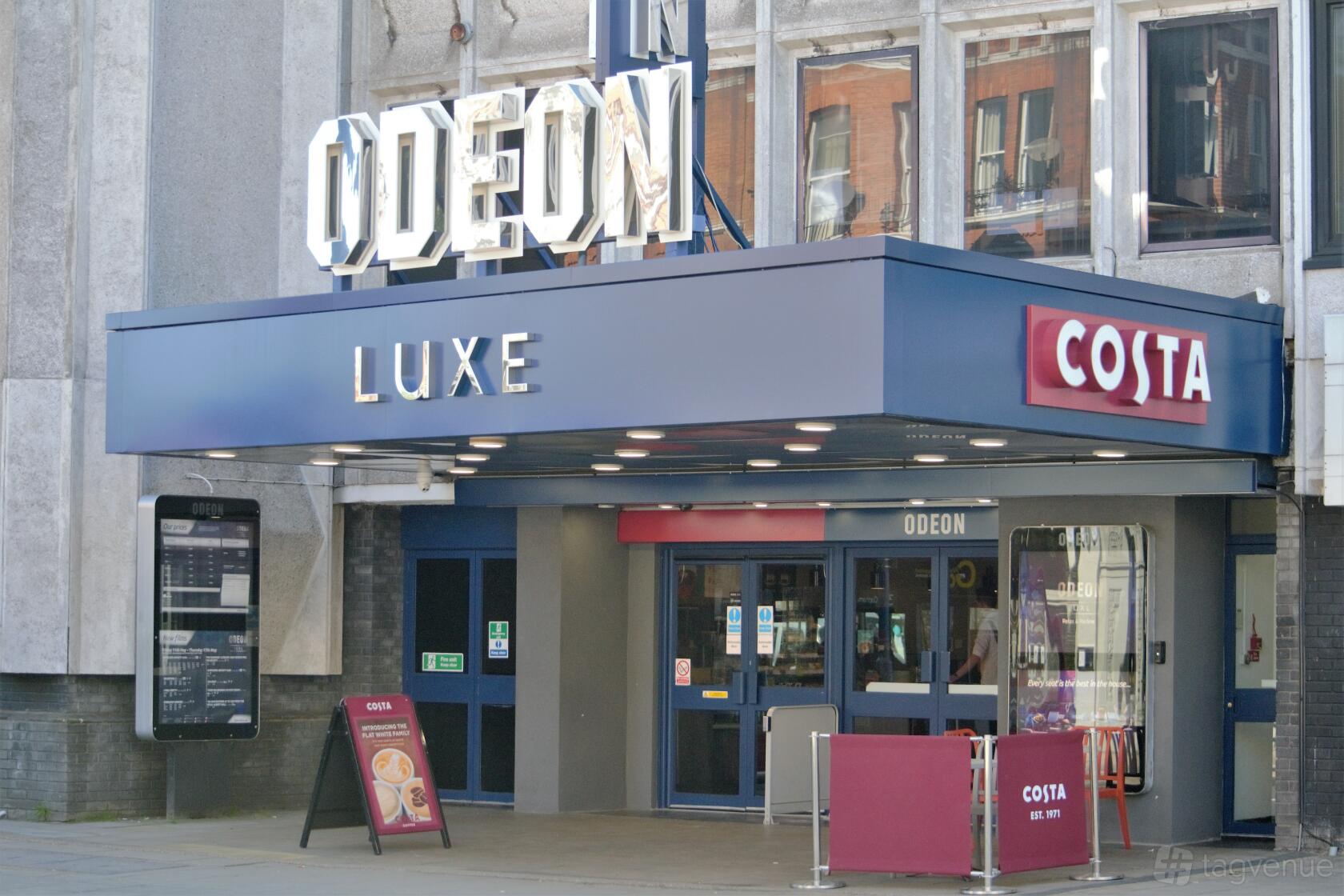 A cinema entrance with a large illuminated marquee, blue canopy, and Costa Coffee signage at ODEON LUXE Putney.