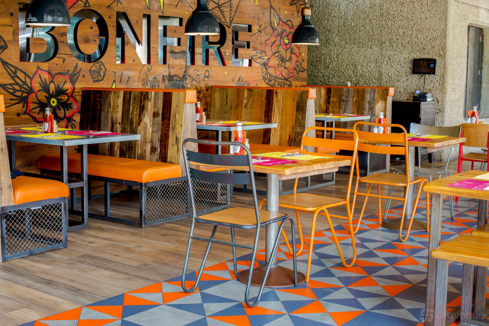 A restaurant area with orange cushioned booths, wooden tables, and industrial pendant lights at Barbican.