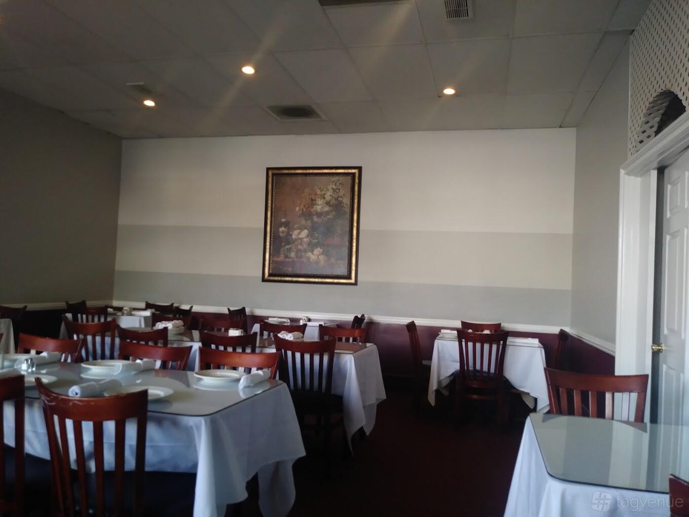 A restaurant dining room with wooden chairs, tables set with white linens, and a floral painting at CF Food Kitchen.