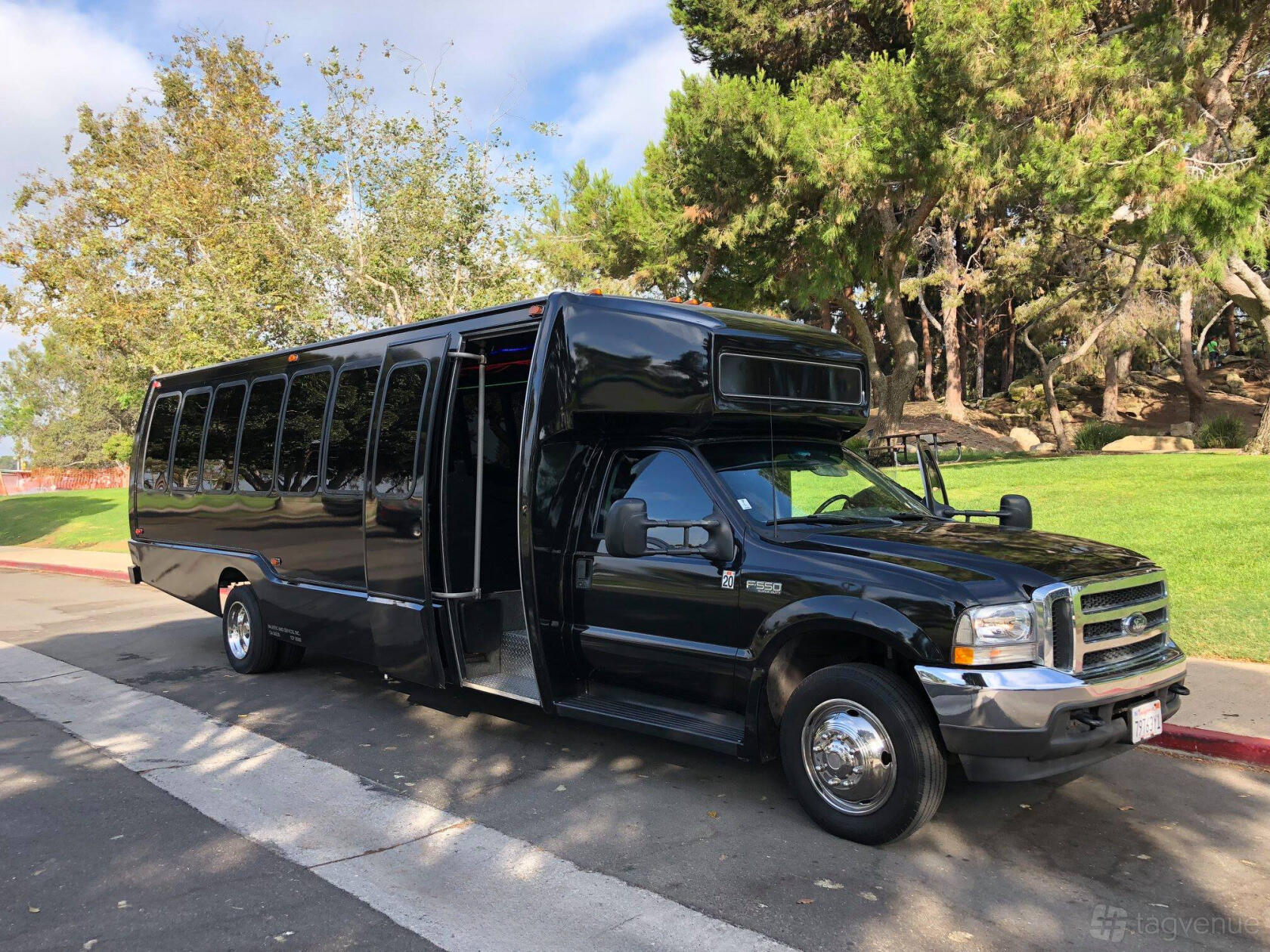 A black party bus parked curbside with tinted windows and open door at Party Bus 4 Us.