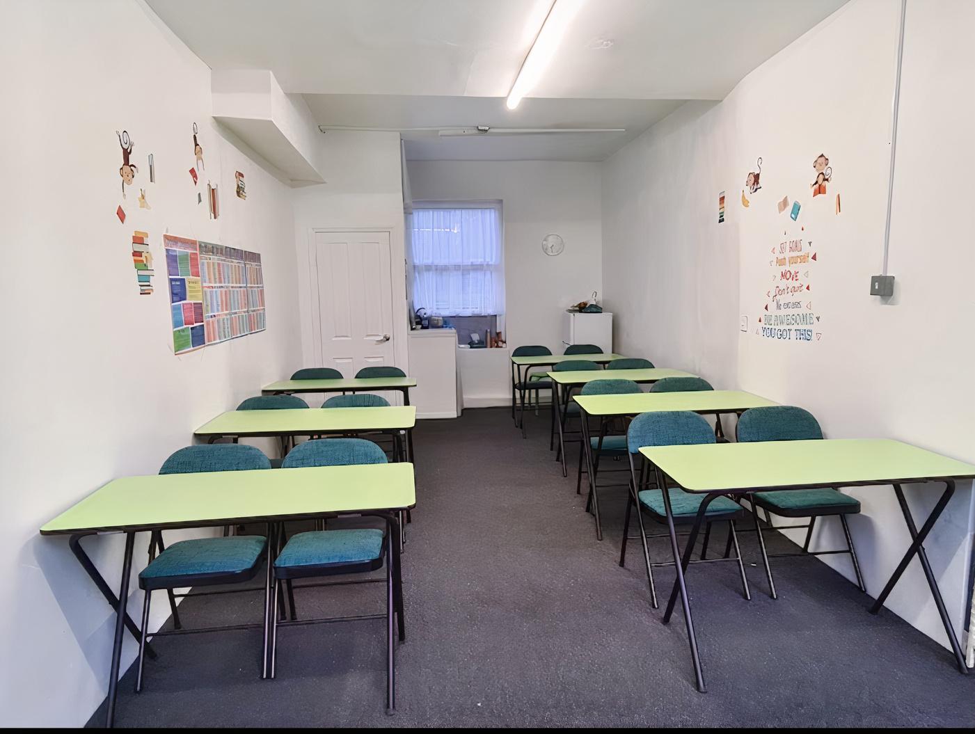 A meeting room with green tables, blue chairs, wall charts, and educational posters at Al Kareem Tutors.