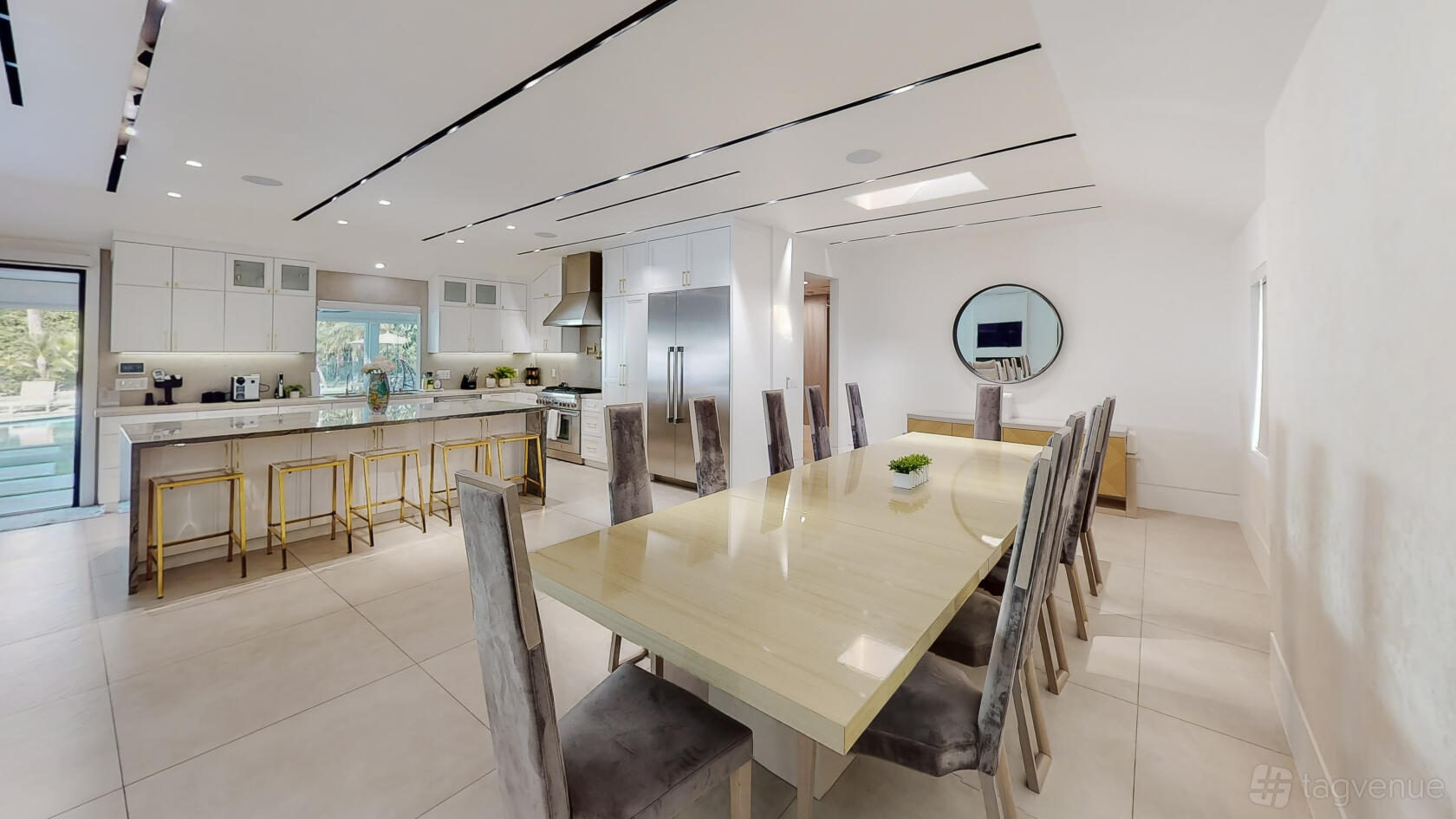 An event venue with a long dining table, velvet chairs, and an open kitchen with barstools at Palm Springs Vacation Home in LA.