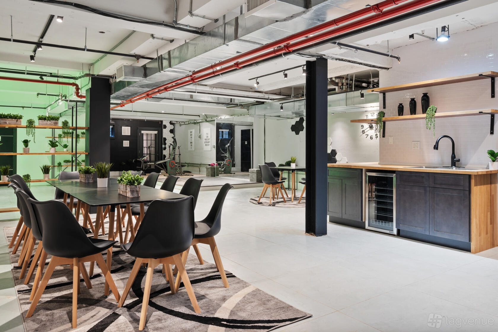 A photo studio with open workspace, long tables with black chairs, potted plants, and a kitchenette at The Recap Group.