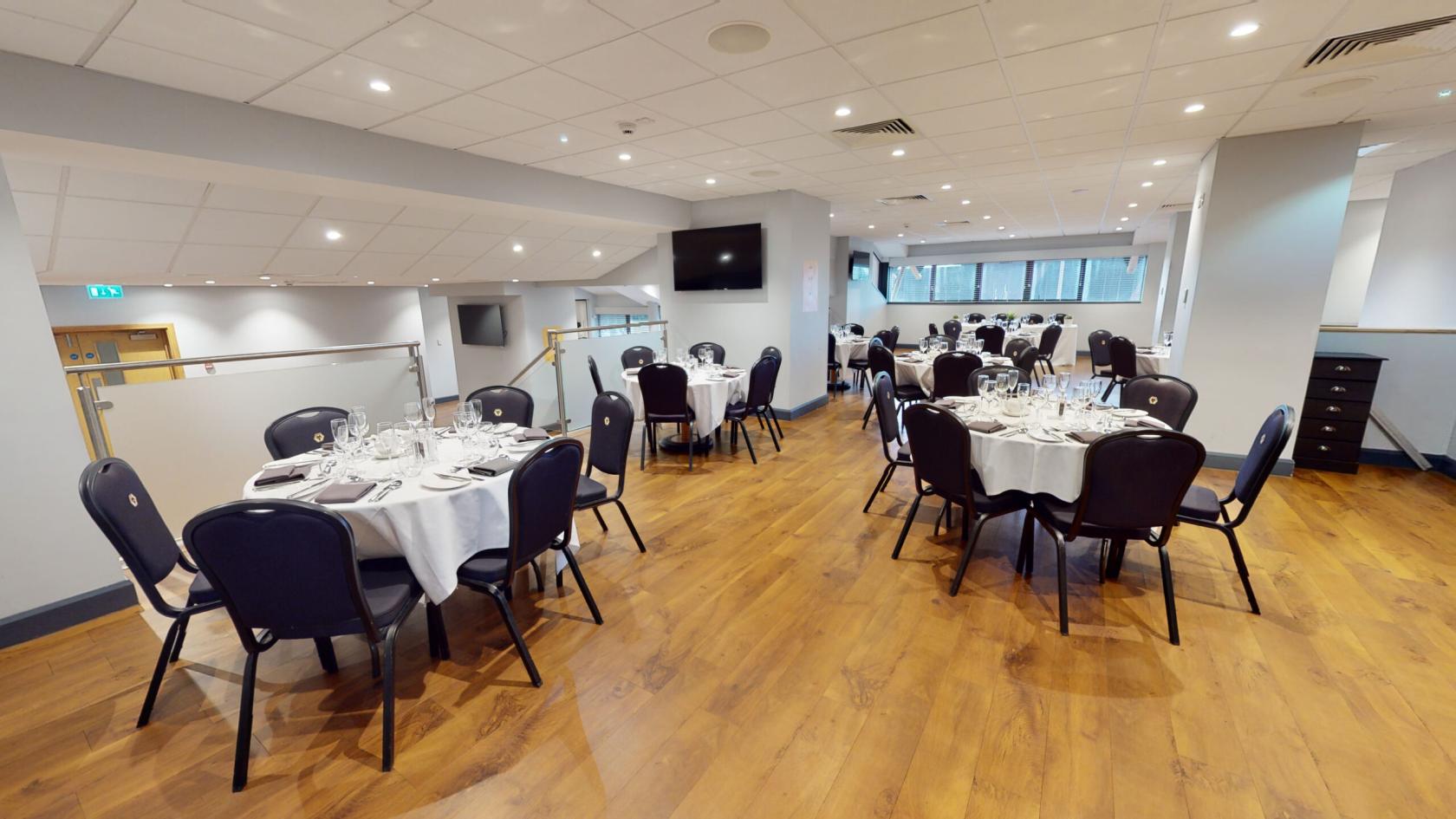 A boardroom with round tables set with white linens and glassware on wooden floors at Molineux Stadium.