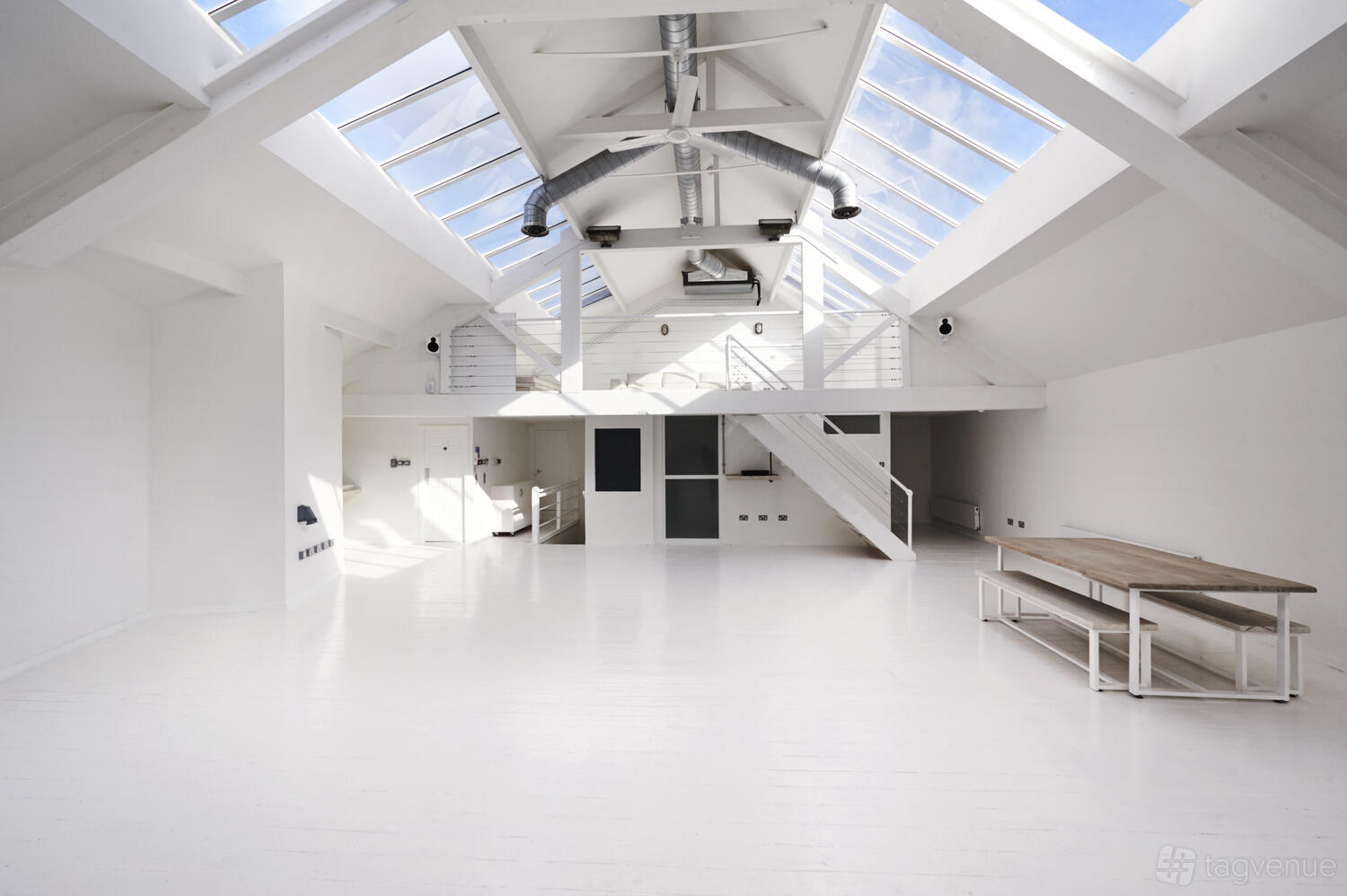 An event space with white floors, skylights, exposed beams, and a wooden table at fivefourstudios The Loft.