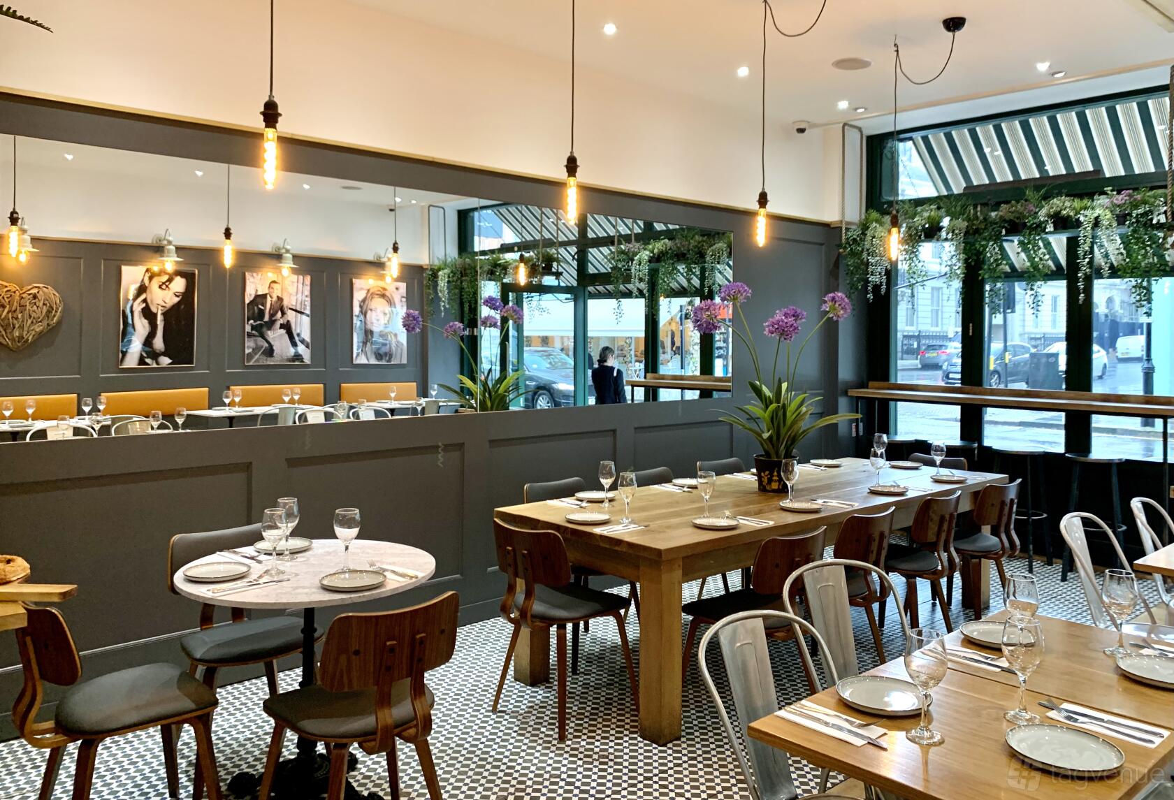 A restaurant with wooden tables, hanging pendant lights, tiled floors, and large windows at Zack's South Kensington.