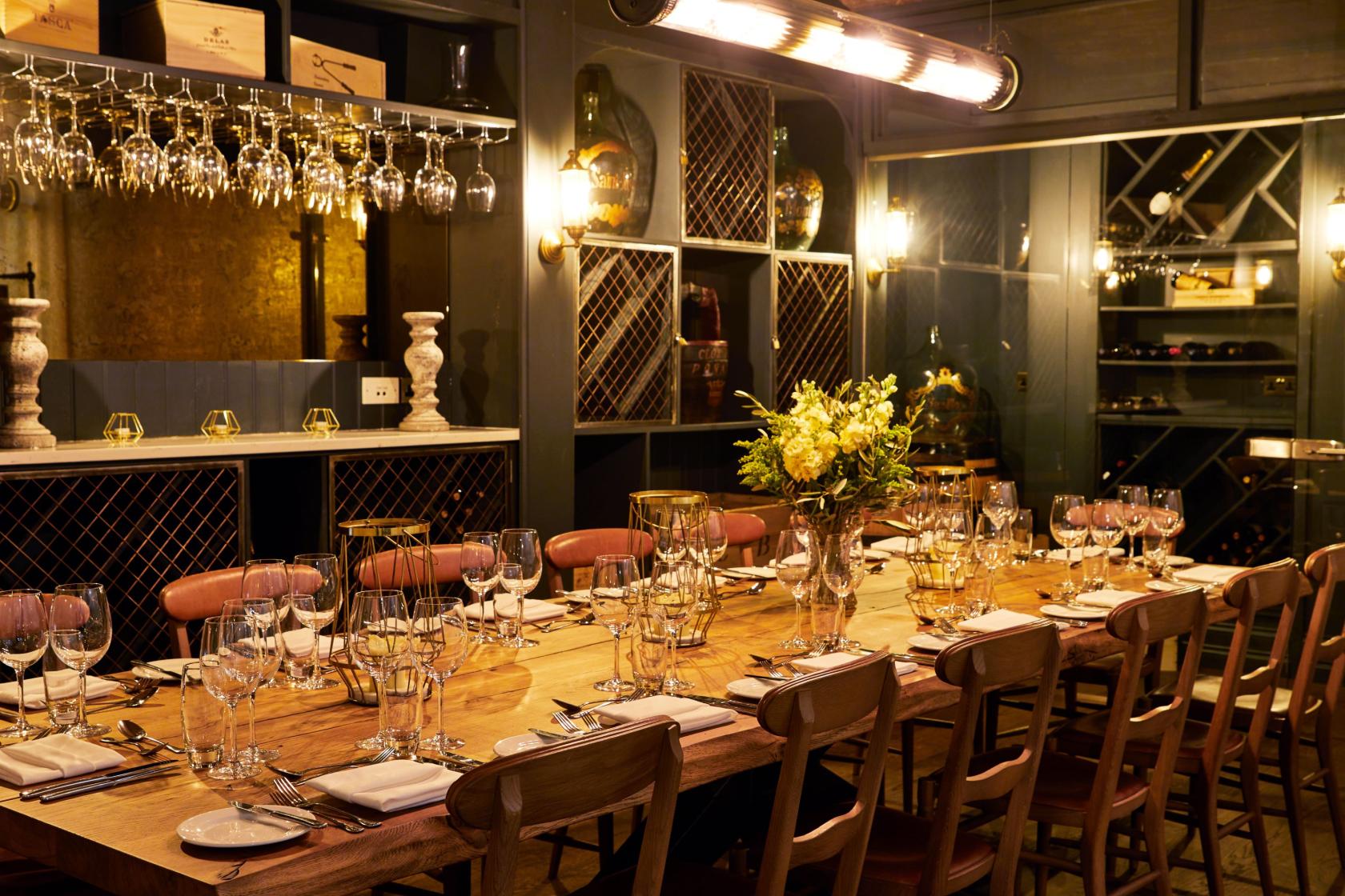 A hotel dining room with a long wooden table, hanging wine glasses, and wall-mounted wine racks at King Street Townhouse.