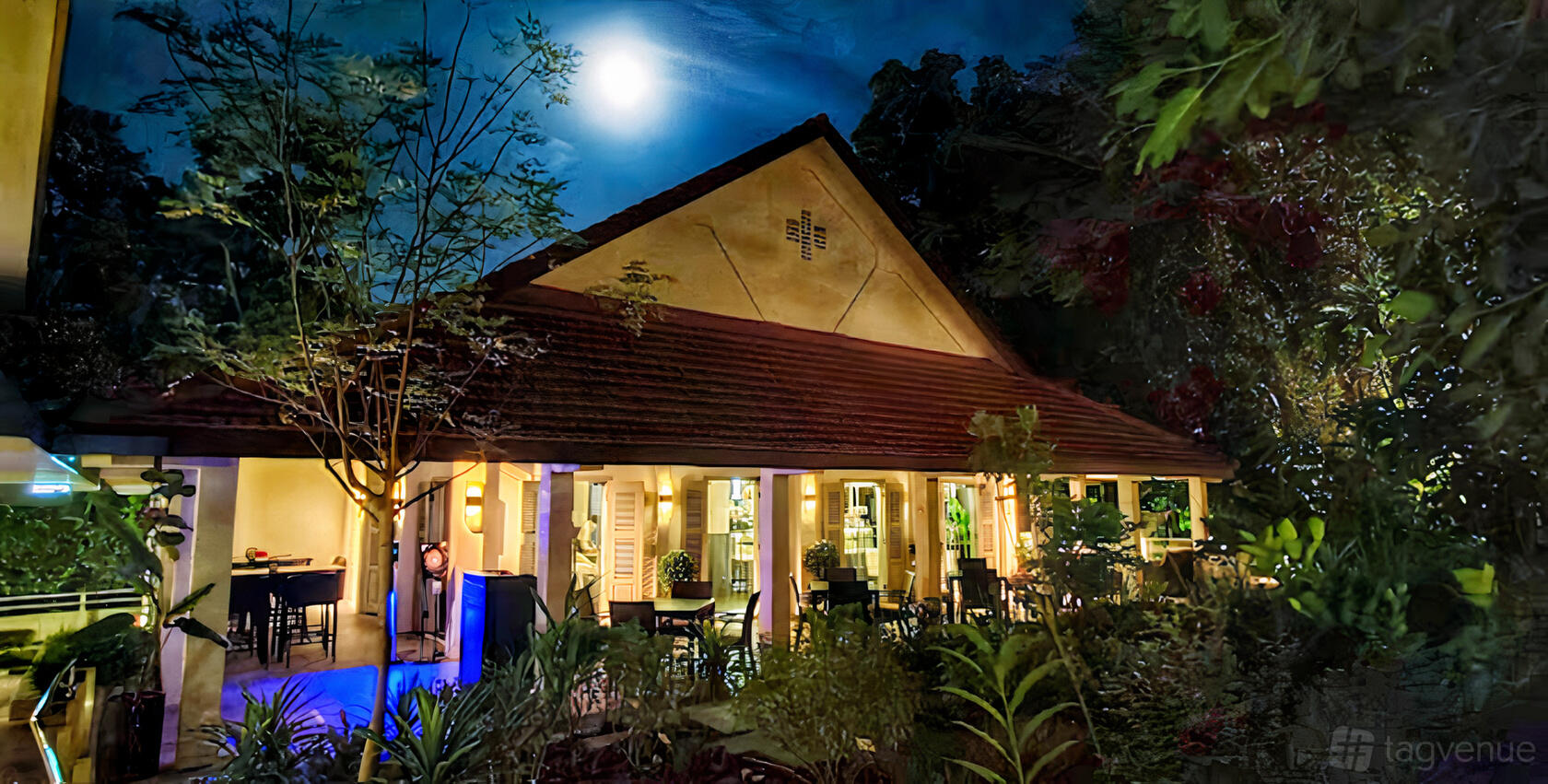 A restaurant with an outdoor patio, lush greenery, and warm lighting under a moonlit sky at Quentin's Bar and Restaurant.