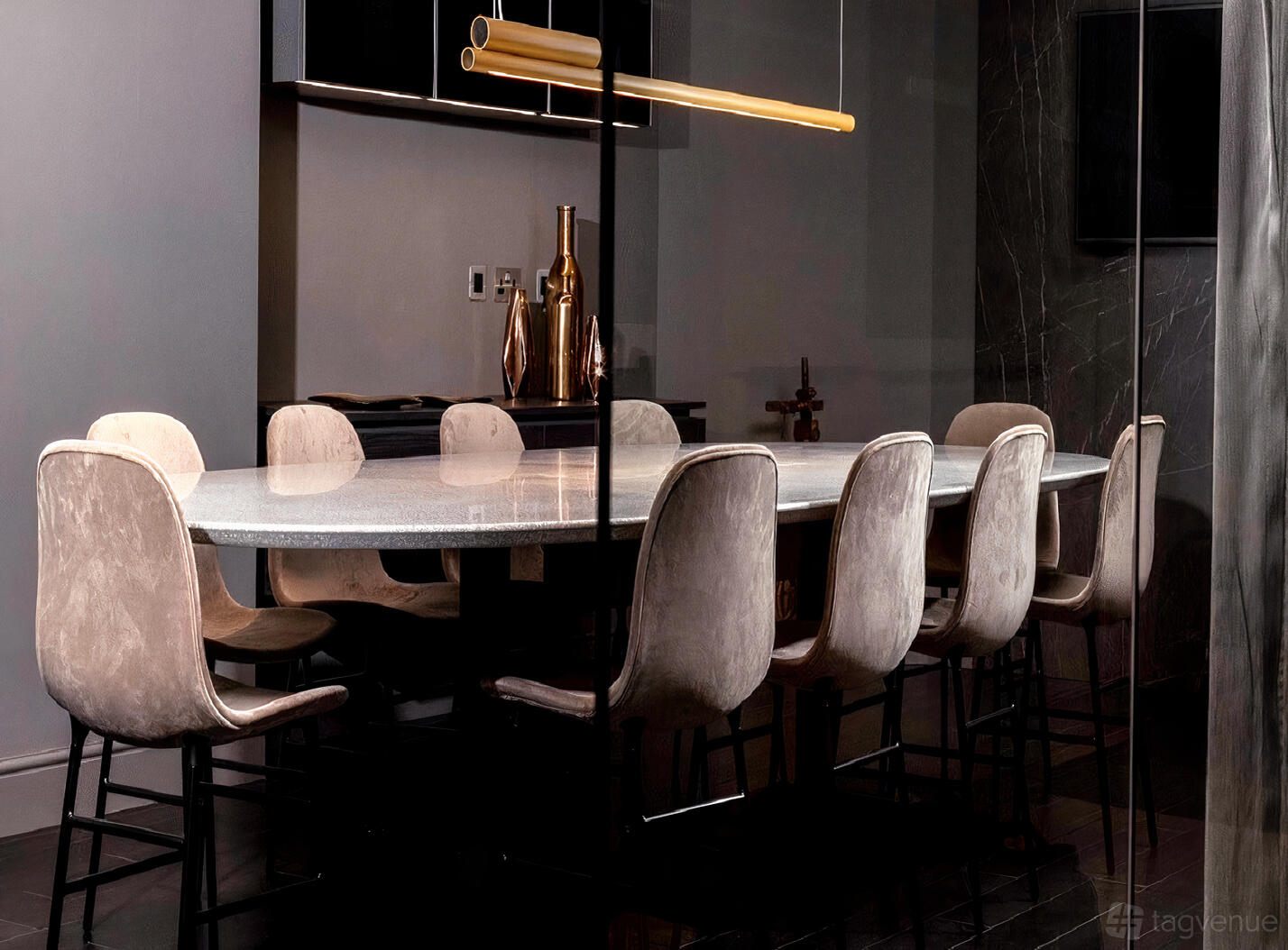 A meeting room with a long marble table, plush beige chairs, and golden vases on a side counter at Halcyon.