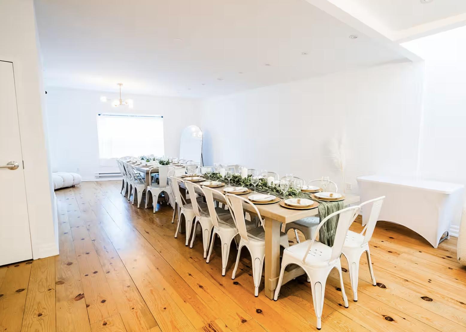 An event venue with long wooden tables, white chairs, and natural light from a large window at Leaside Studio.