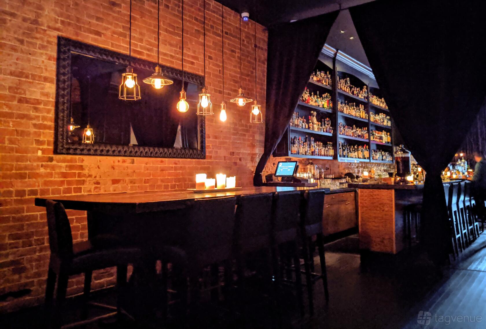A cocktail bar with exposed brick walls, pendant lighting, and a backlit bottle display at BarChef Events.