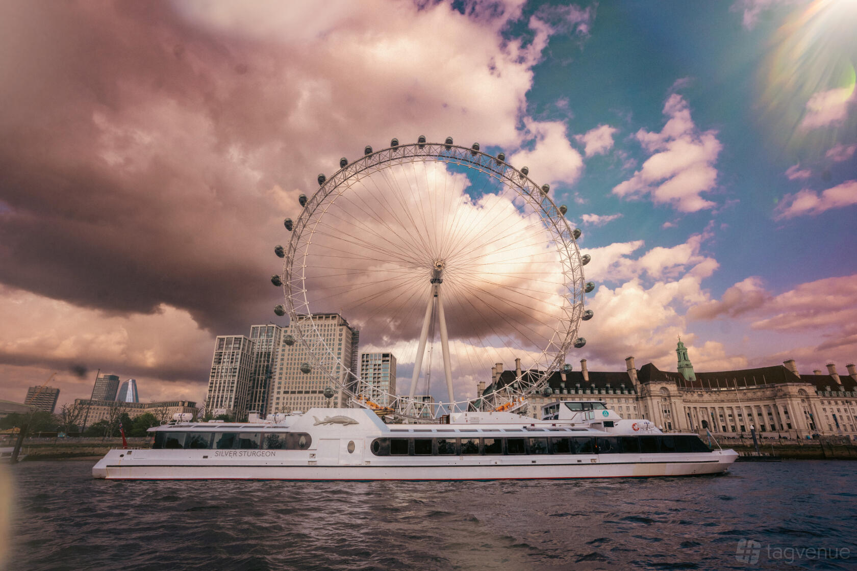 A yacht with large windows cruising on the river near the London Eye at Woods Silver Fleet.