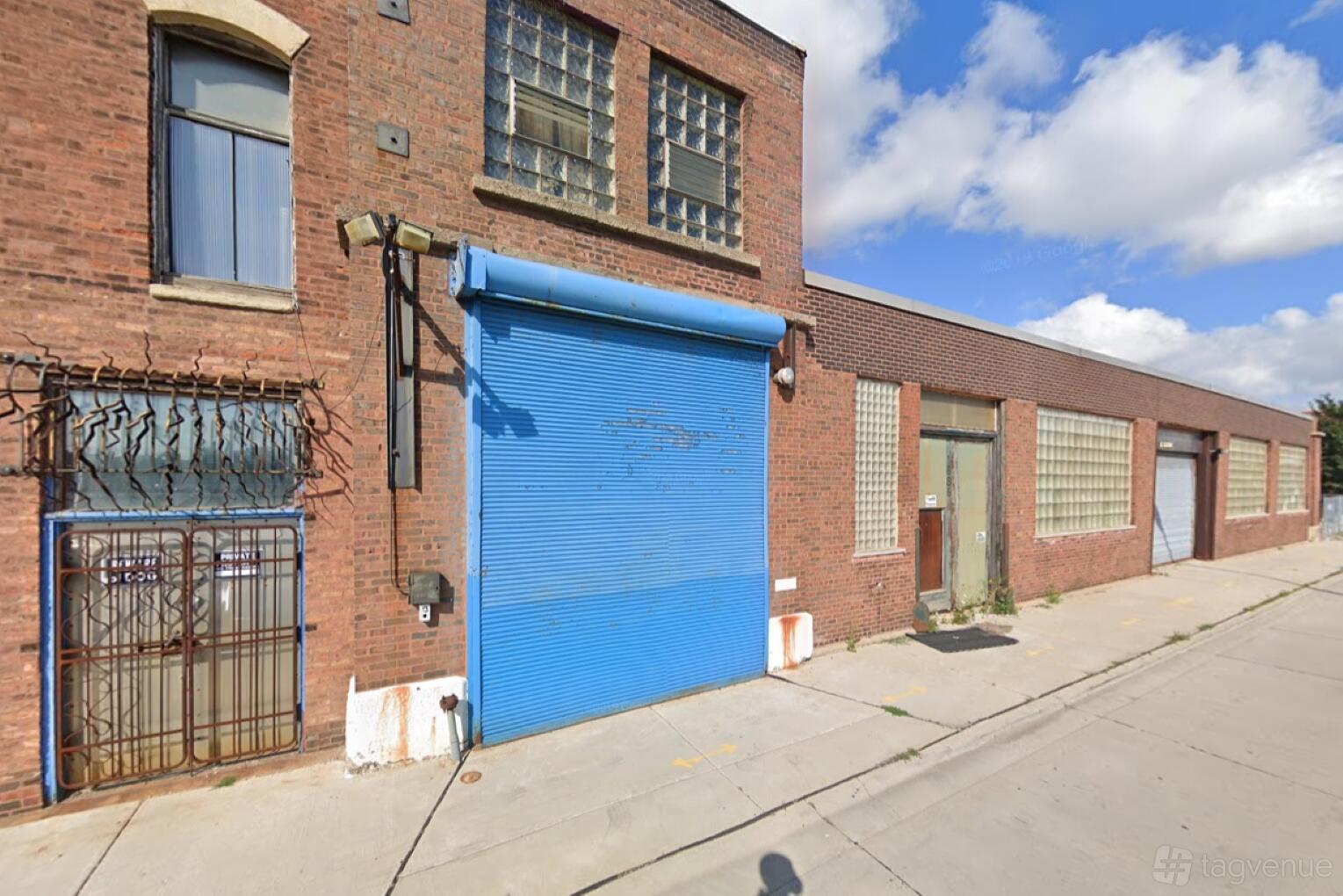 An apartment building with a blue roll-up door, brick facade, and glass block windows at Charcoal Factory Loft.