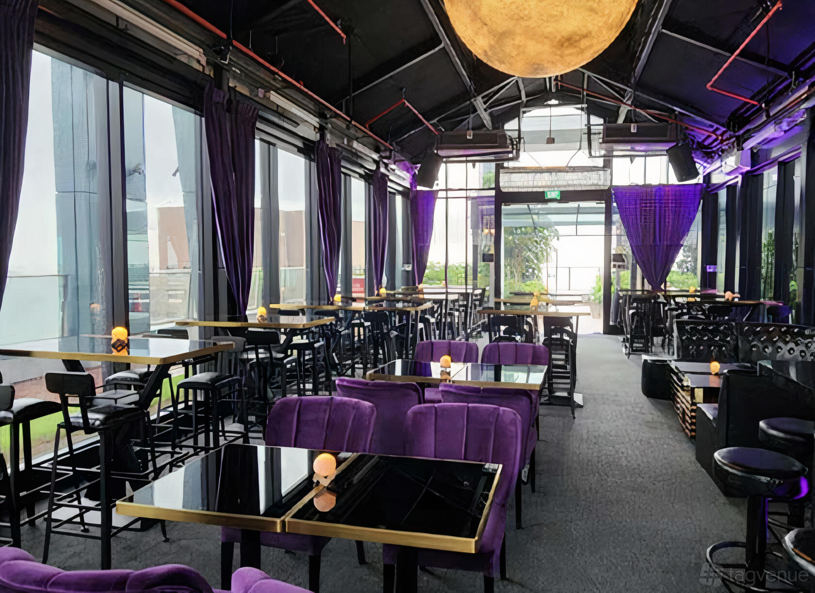 An indoor bar with floor-to-ceiling windows, purple velvet seating, and glass tables at Moon Rooftop Bar and Lounge.