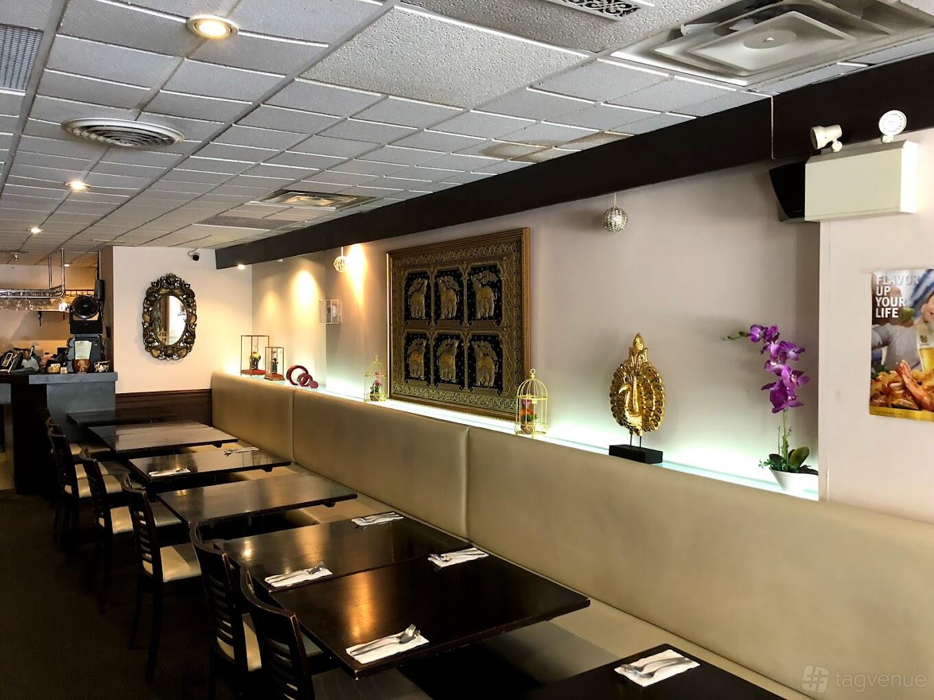 A restaurant dining area with dark wood tables, cushioned bench seating, decorative Thai artwork, and wall-mounted lighting at Thai House Cuisine - Toronto.