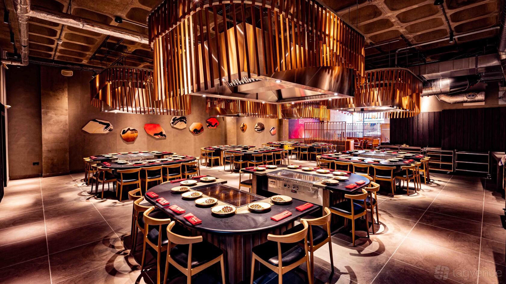 A restaurant with teppanyaki tables, overhead wooden slat fixtures, and wall-mounted fish art at Benihana.