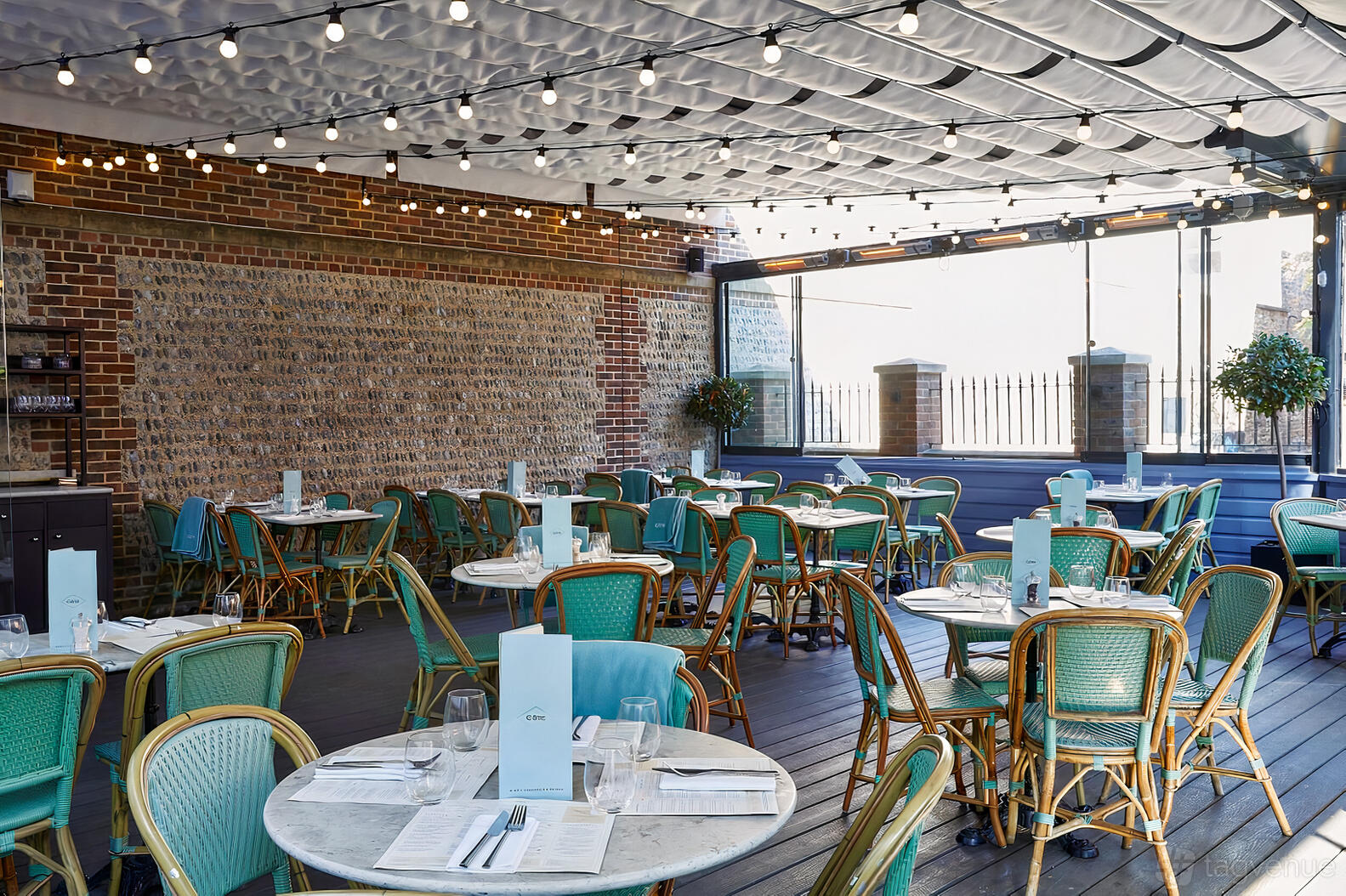 A restaurant terrace with round marble tables, teal chairs, and string lights at Côte Brasserie Brighton.
