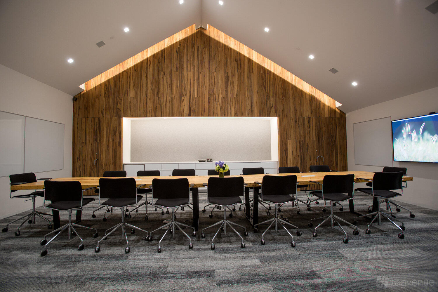 A conference room with a long wooden table, black chairs, and a wood-paneled accent wall at Project Farmhouse.
