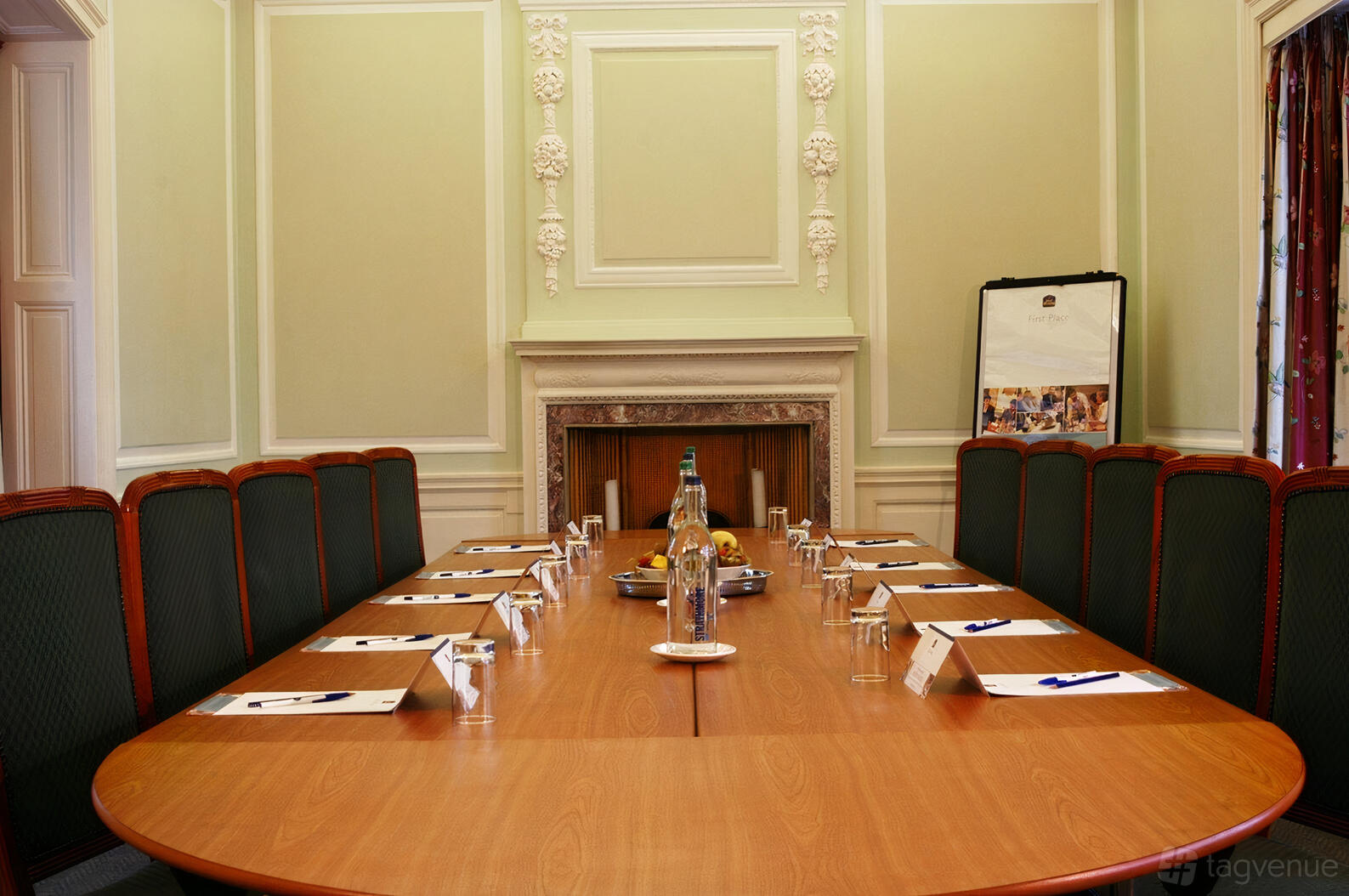 A meeting room with a long wooden table, high-backed chairs, ornate wall molding, and a fireplace at Keavil House Hotel.