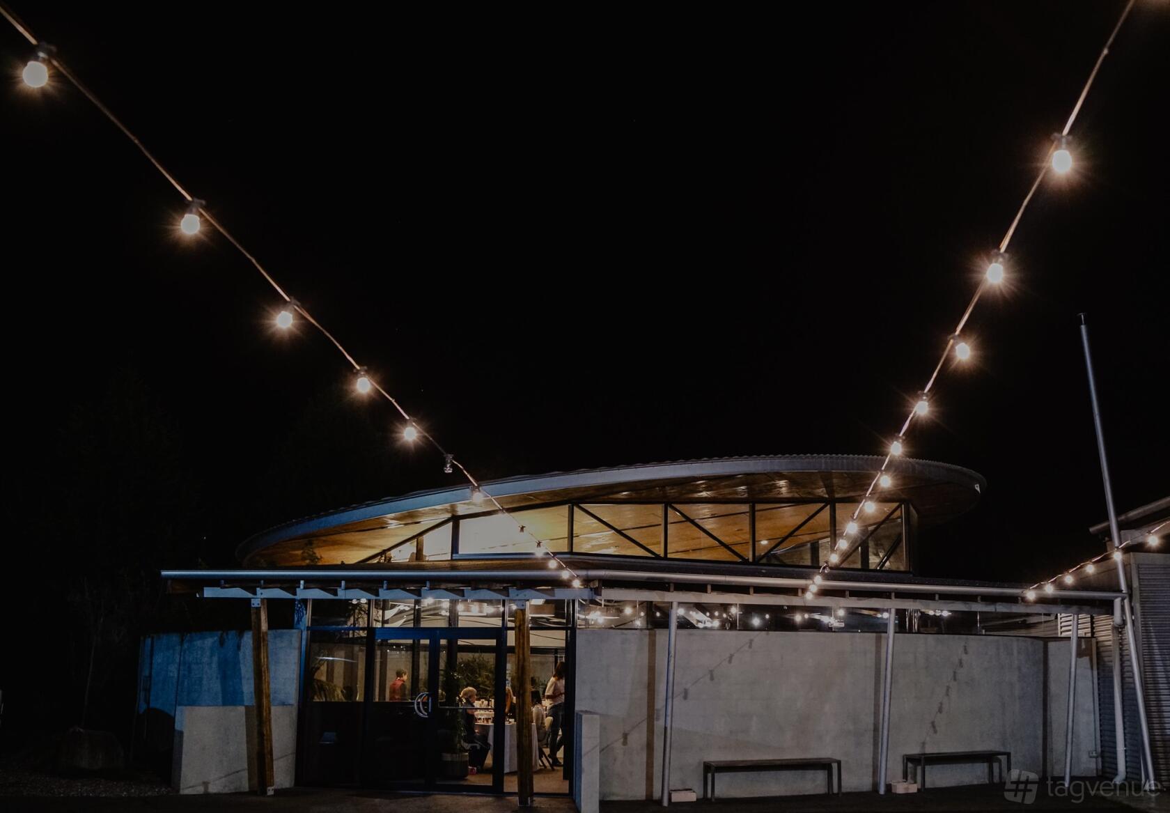 An event venue with string lights overhead and large windows at Tailrace Centre