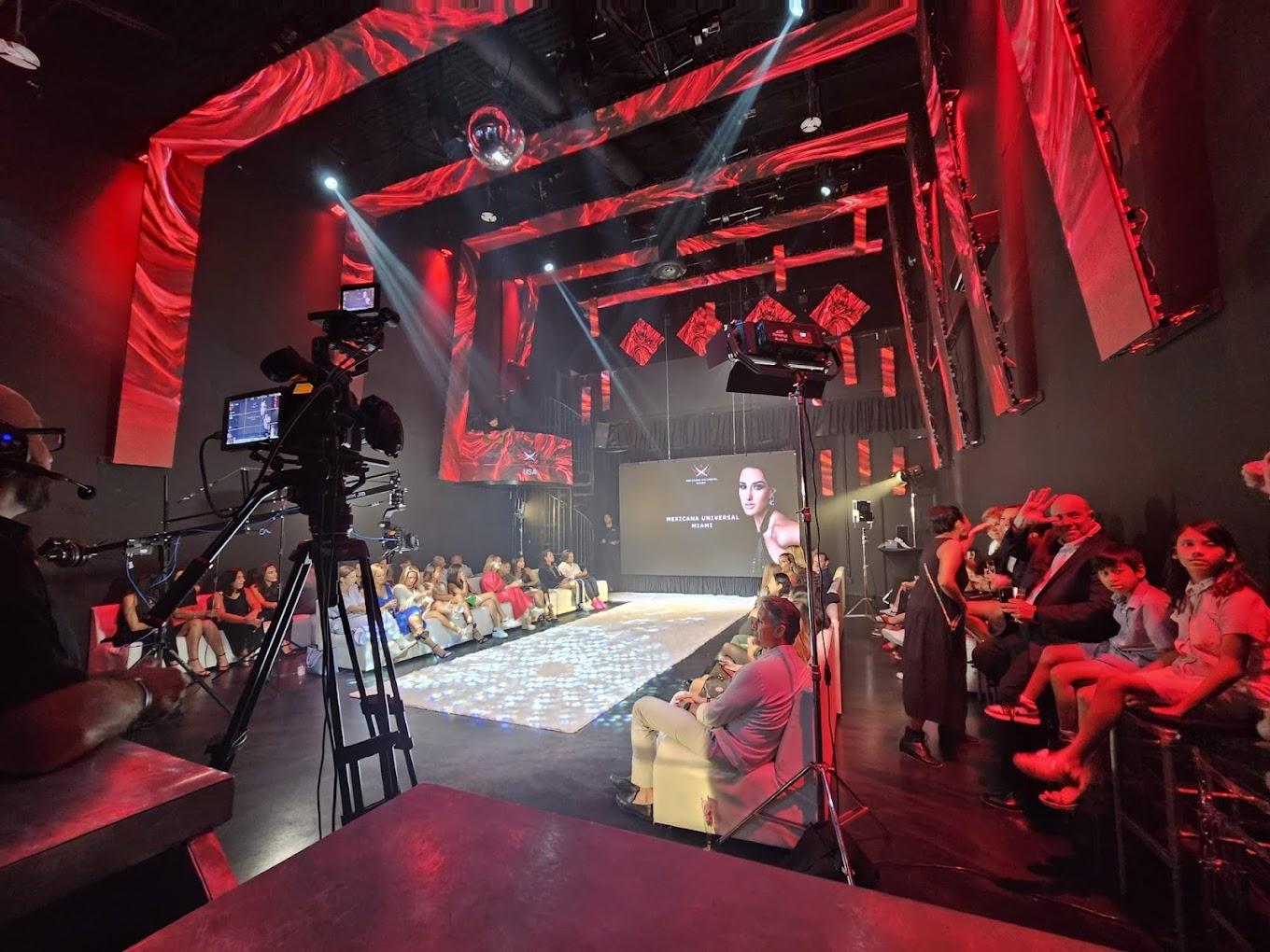 A nightclub with a lit runway, red uplighting, and audience seating on both sides at CUZ Miami Venue.