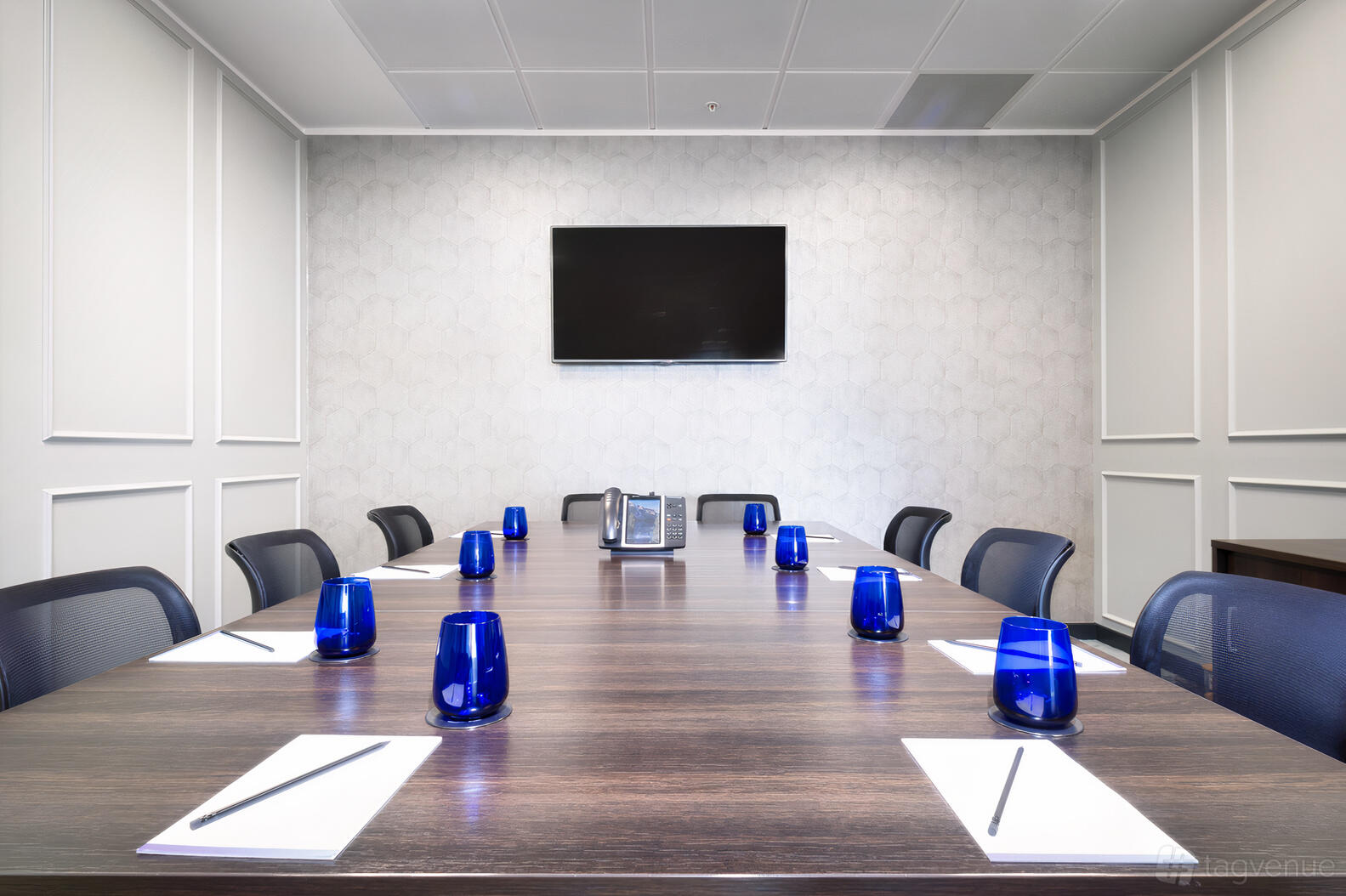 A meeting room with a long wooden table, blue glasses, notepads, and wall-mounted TV at Landmark: Beaufort House, Aldgate.