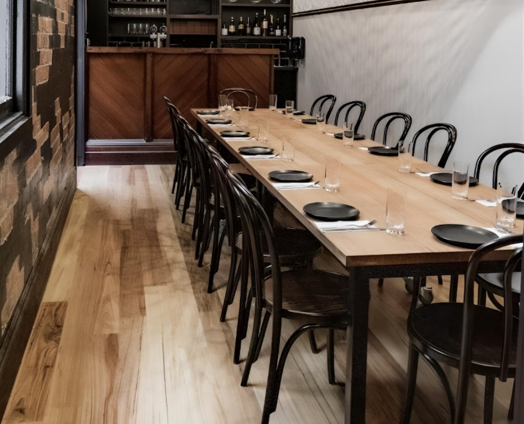 A dining room with a long wooden table, black chairs, and brick accent walls at Sidebar