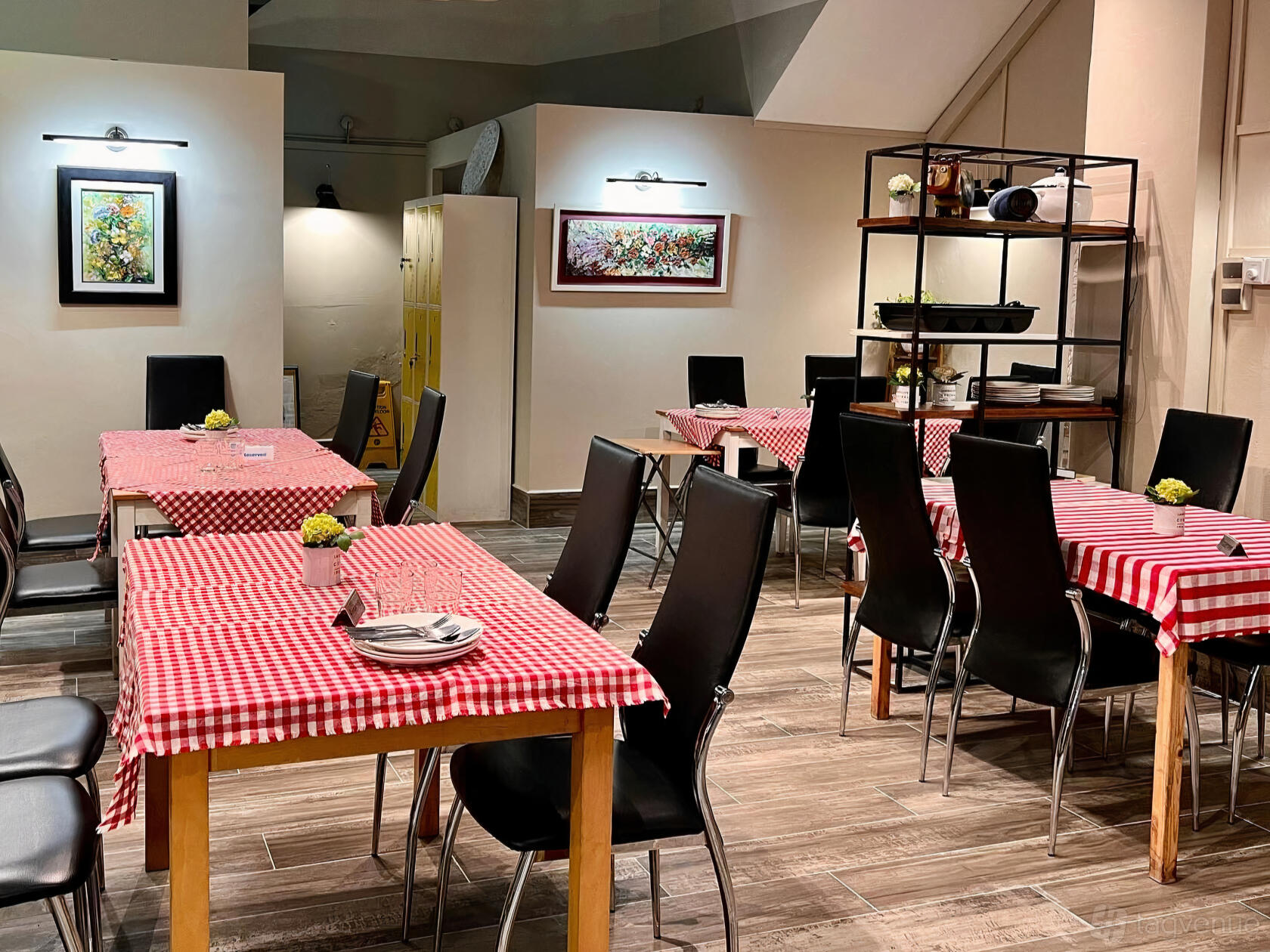 A restaurant dining area with red checkered tablecloths, black chairs, wall art, and wooden flooring at Micasa Kitchen and Bar.