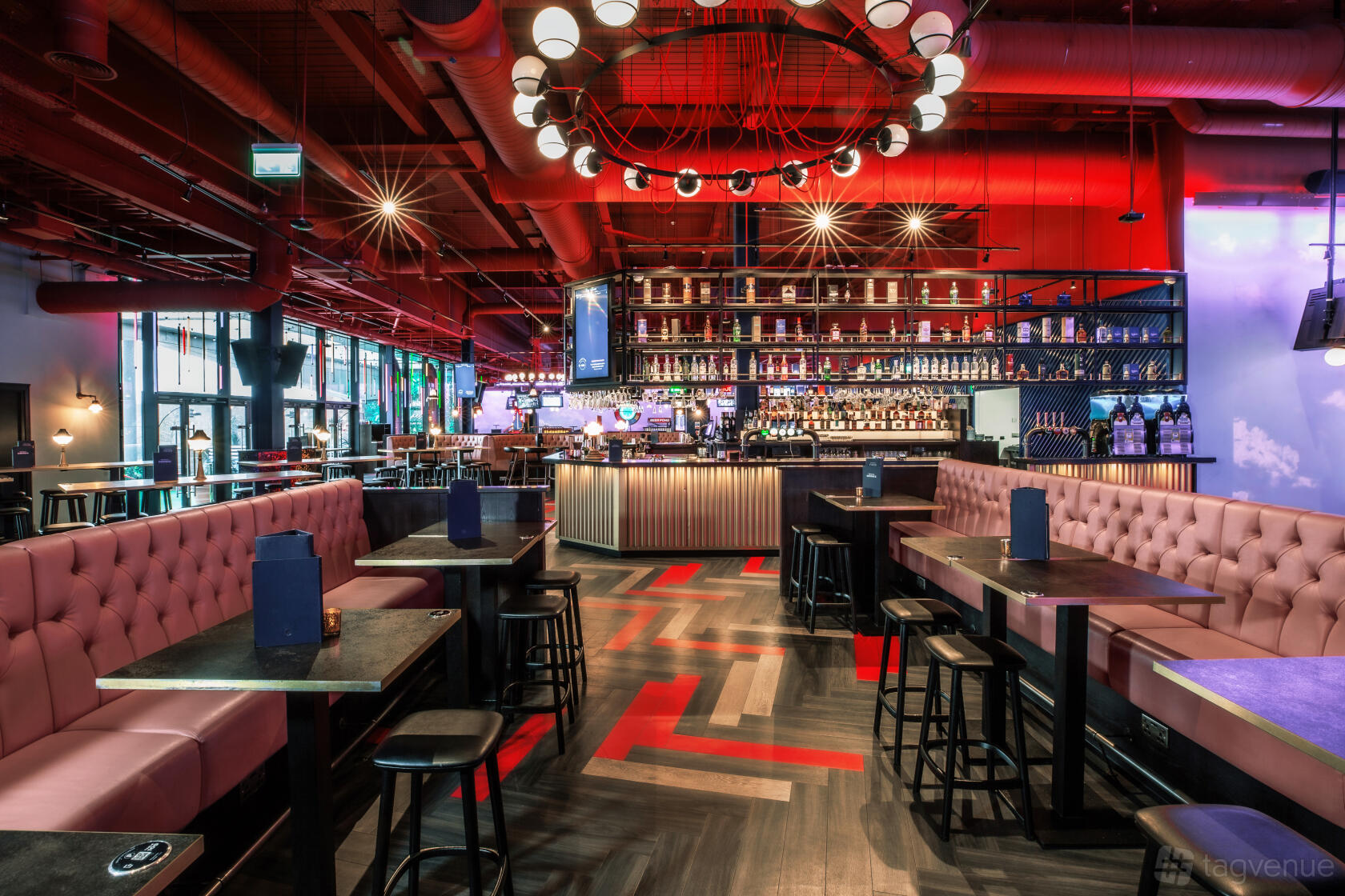 An event venue with tufted banquette seating, high tables, and a large bar under red lighting at Puttshack Lakeside.